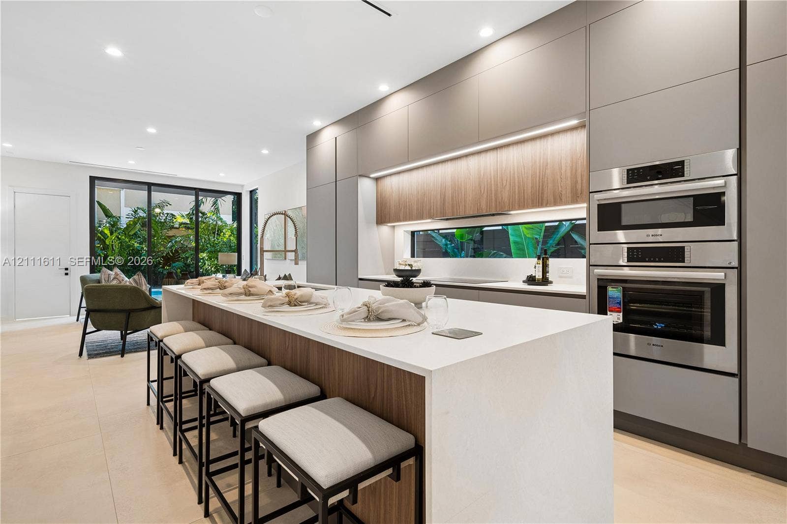 Modern kitchen featuring flat-panel cabinetry, a central island with a solid-surface countertop, integrated stainless steel double wall ovens, recessed lighting, and large-format flooring