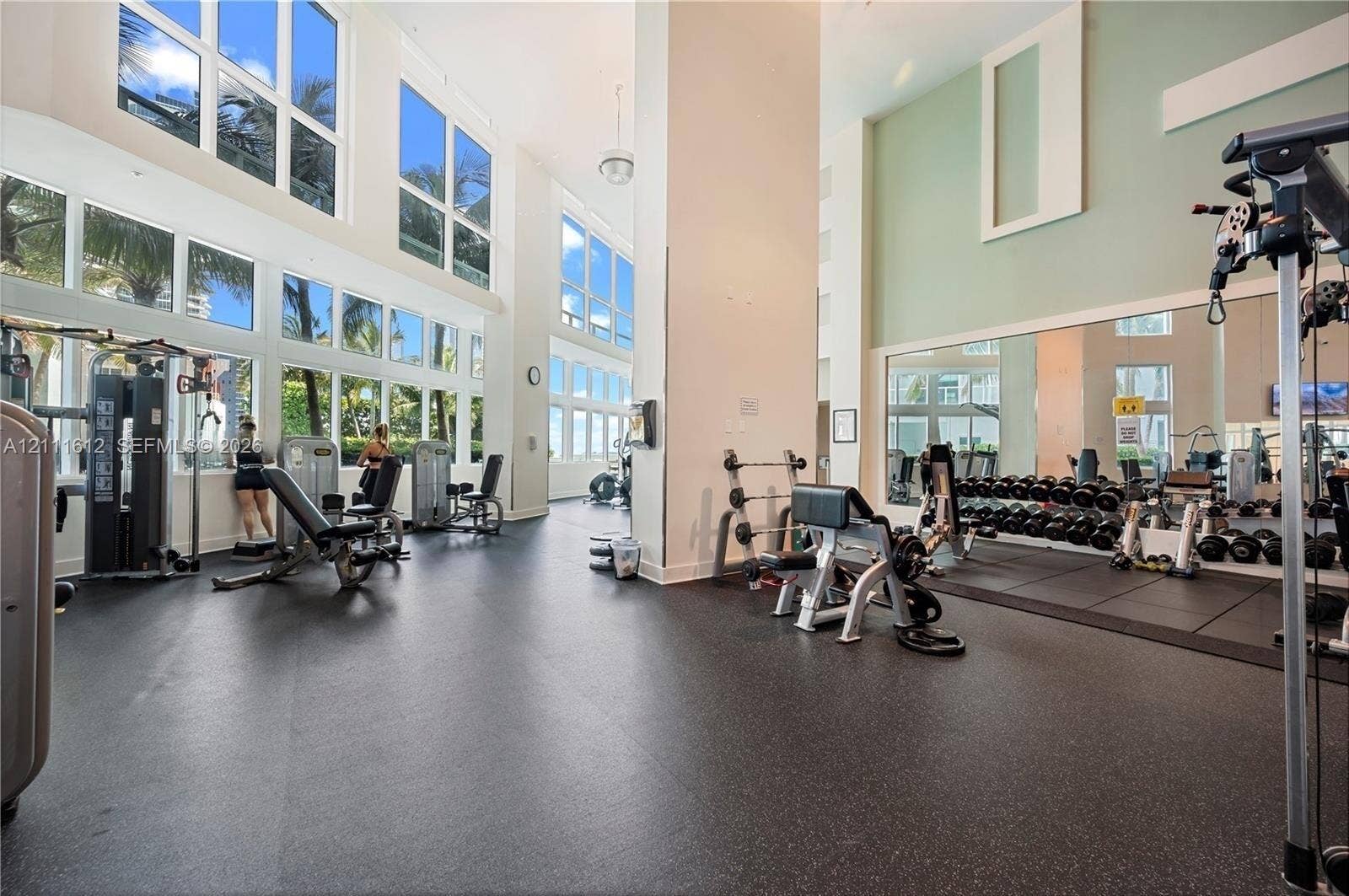 Fitness center featuring double-height ceilings, floor-to-ceiling windows, rubberized flooring, and an expansive wall mirror