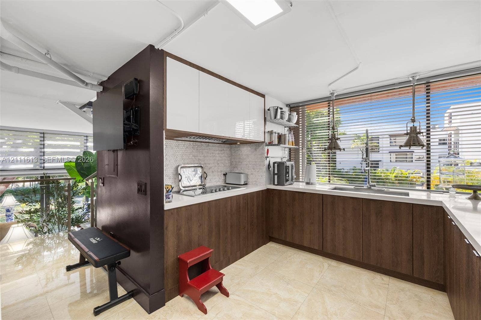 Kitchen featuring two-tone cabinetry with wood-finish lower units and high-gloss upper cabinets, solid-surface countertops, mosaic tile backsplash, and oversized windows with pendant lighting