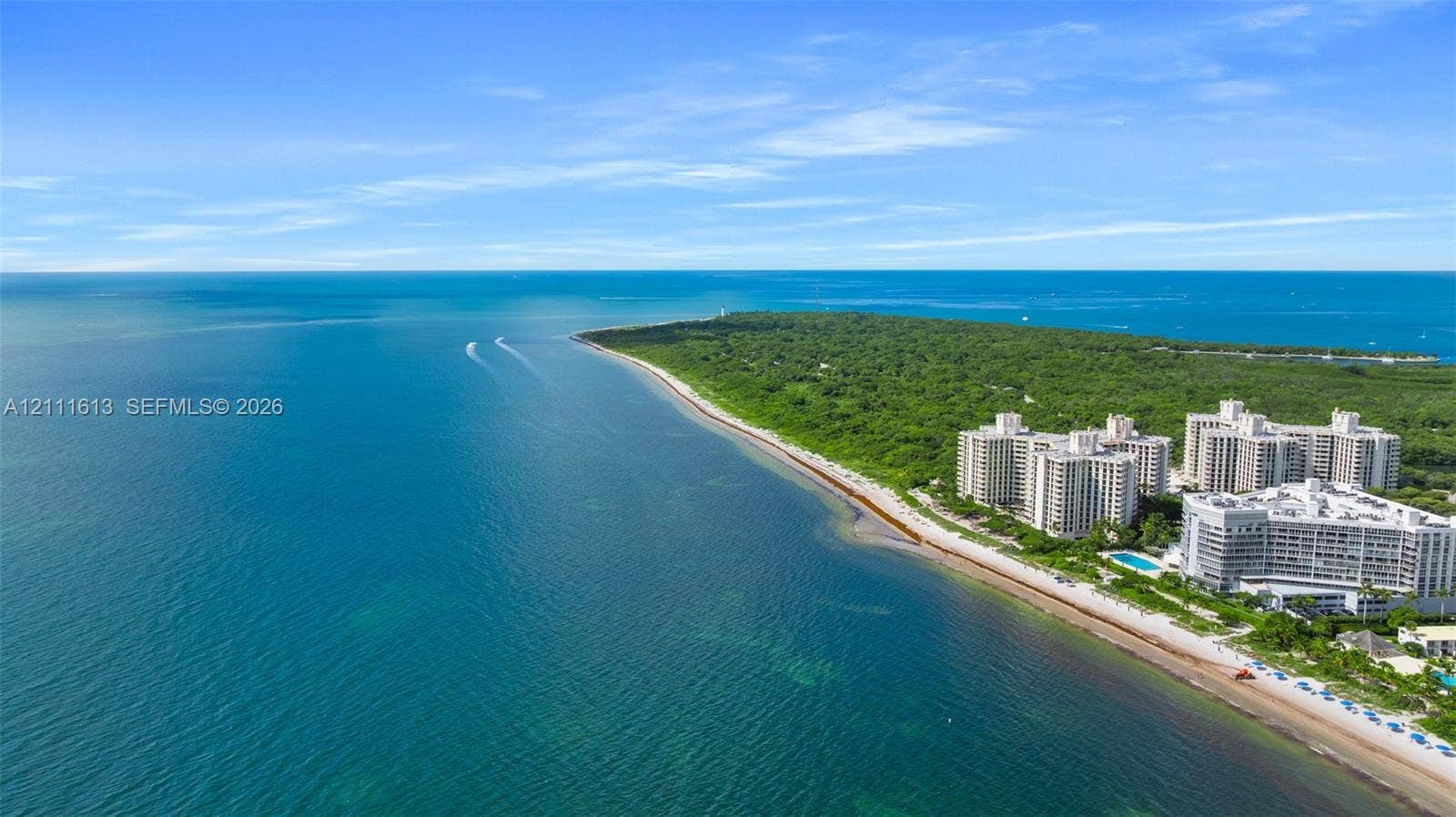 Aerial perspective of coastal multi-story residential buildings featuring immediate proximity to the shoreline and direct access to expansive sandy beach frontage