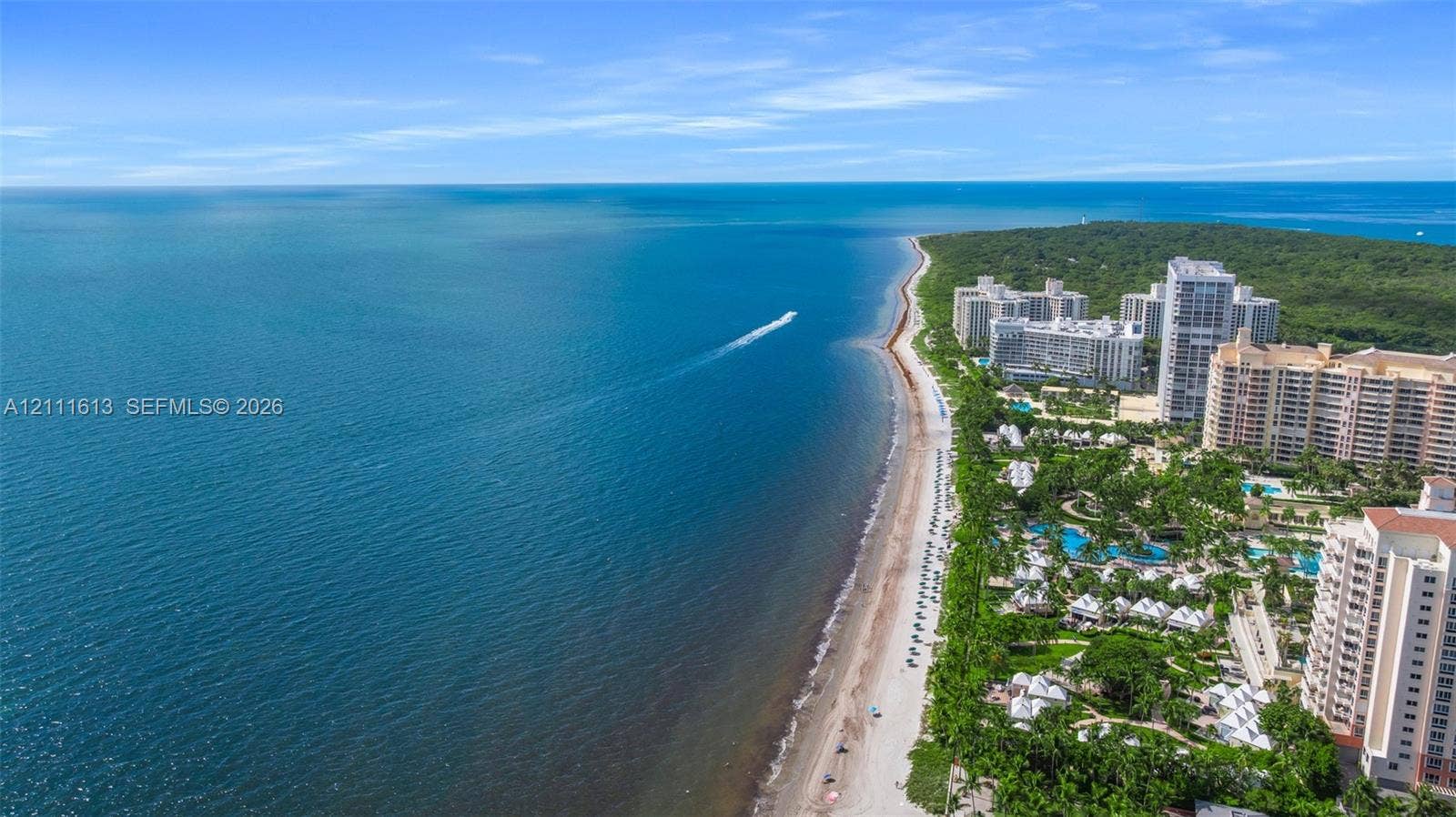 Coastal property featuring direct ocean frontage, expansive sandy beach, and proximity to mid-rise residential structures surrounded by mature tropical landscaping