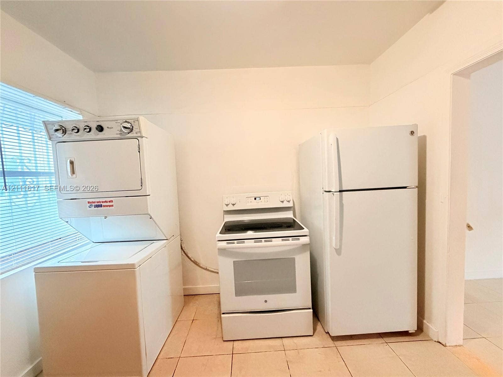 Stacked washer and dryer unit, electric range, and top-freezer refrigerator set upon tile flooring