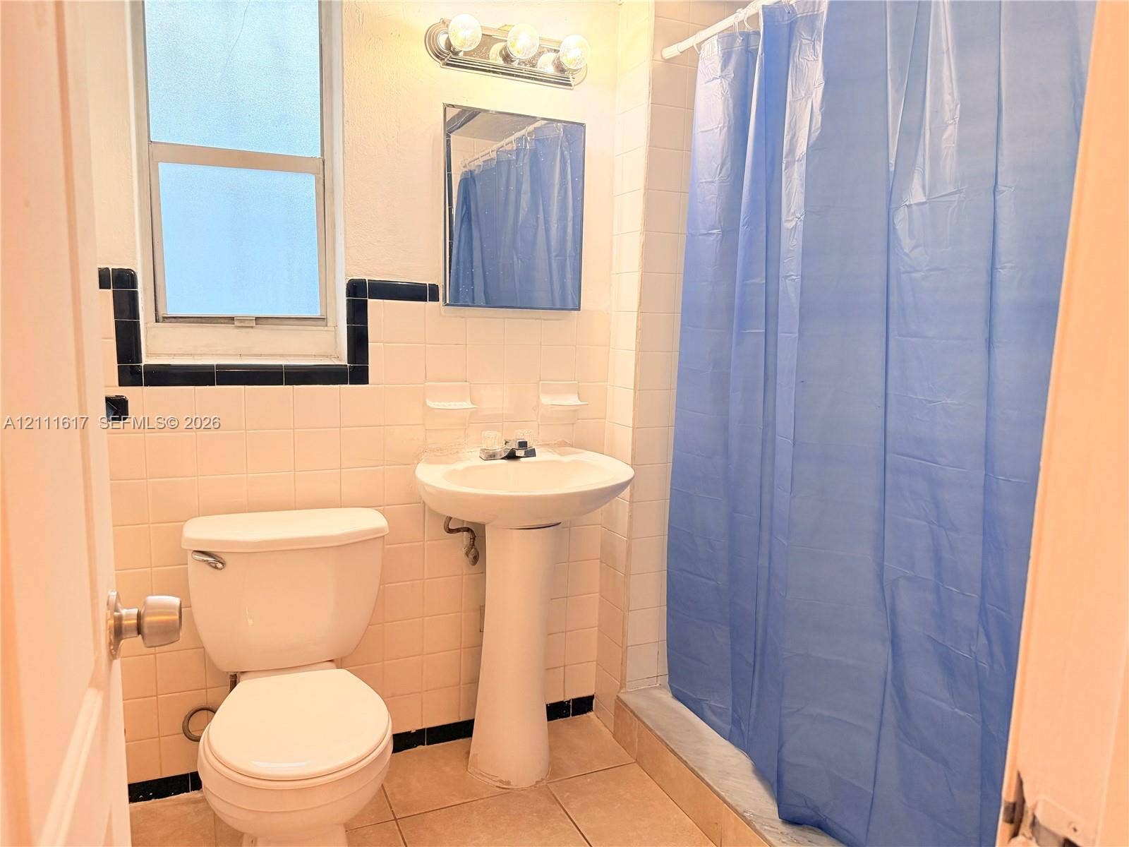 Bathroom featuring a pedestal sink, wall-mounted medicine cabinet, tri-light vanity fixture, and white wall tile with dark decorative accent trim