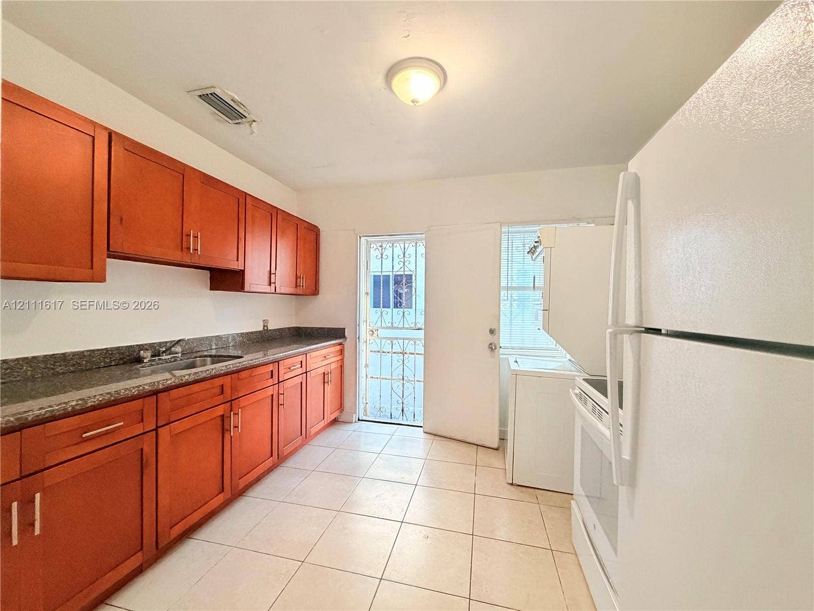 Kitchen featuring wood cabinetry, stone-finish countertops, stainless steel sink, tiled flooring, and exterior access via a metal security door