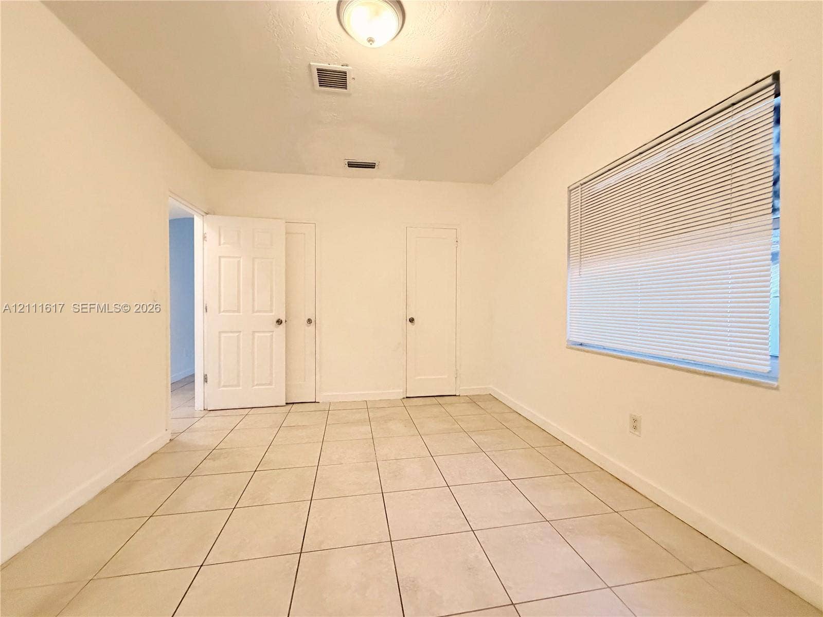 Neutral interior space featuring large-format ceramic tile flooring, two solid-core interior doors, and a single-pane window with integrated horizontal blinds