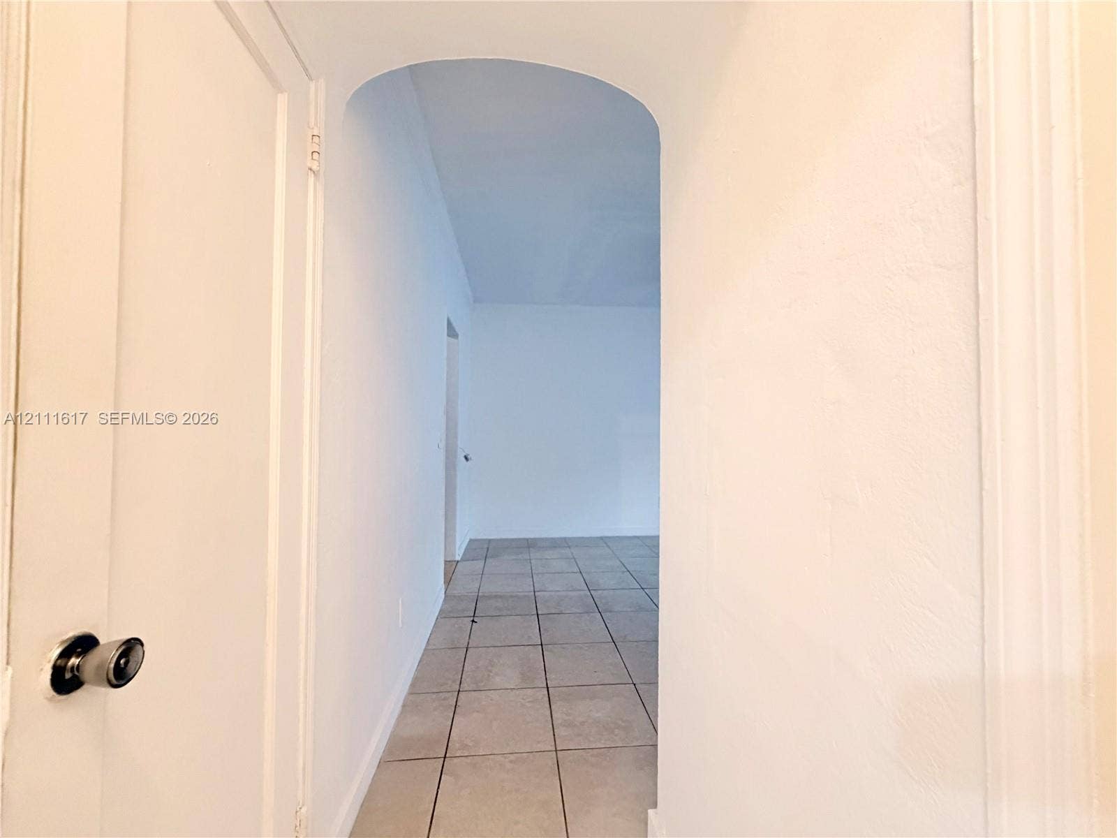 Interior space featuring an arched architectural opening and neutral square floor tiling