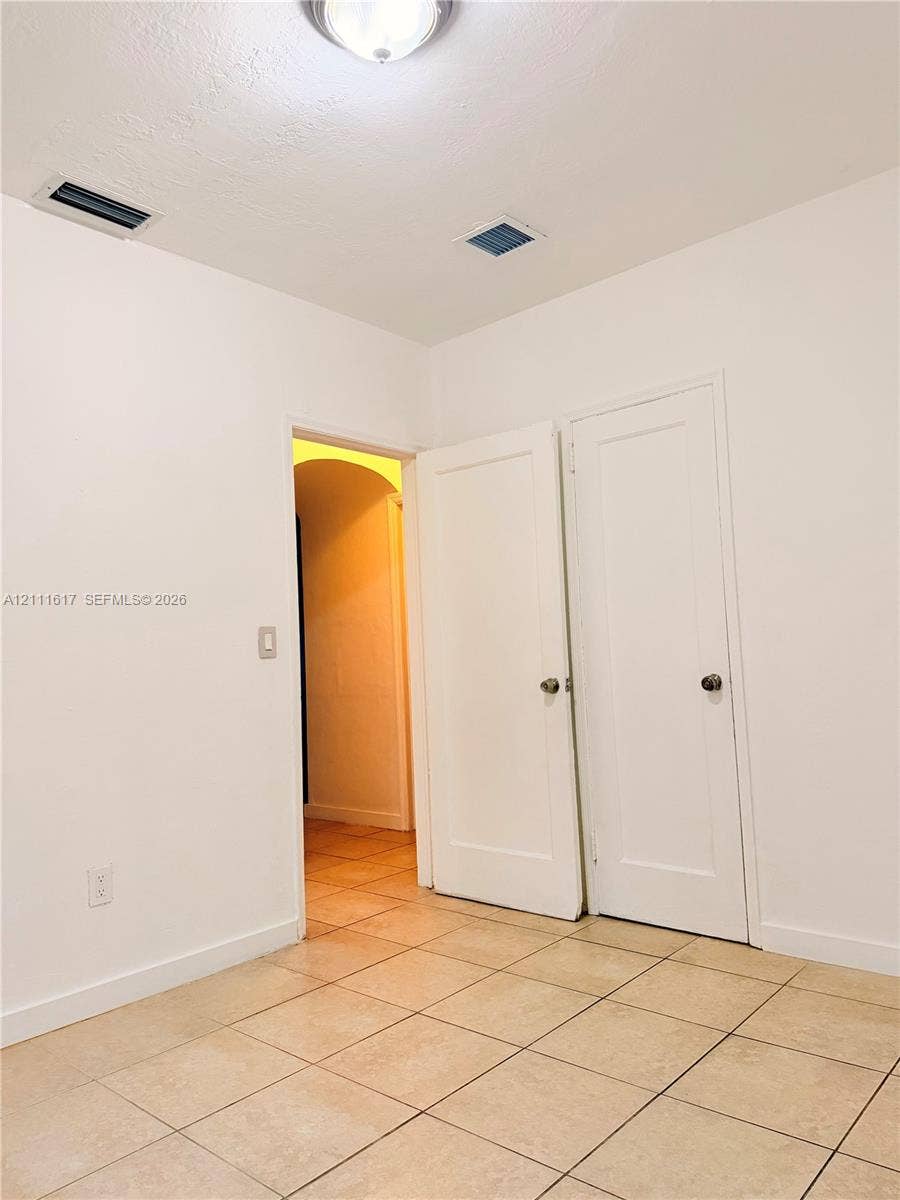 Room with neutral tile flooring, two solid-core interior doors, and arched entryway