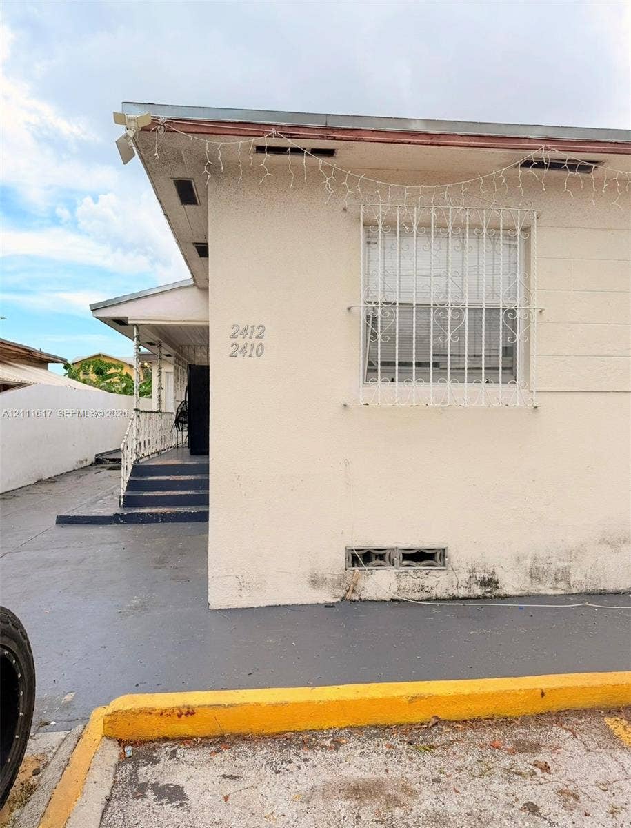 Exterior featuring light-toned masonry, metal window security grilles, concrete steps, and a concrete driveway