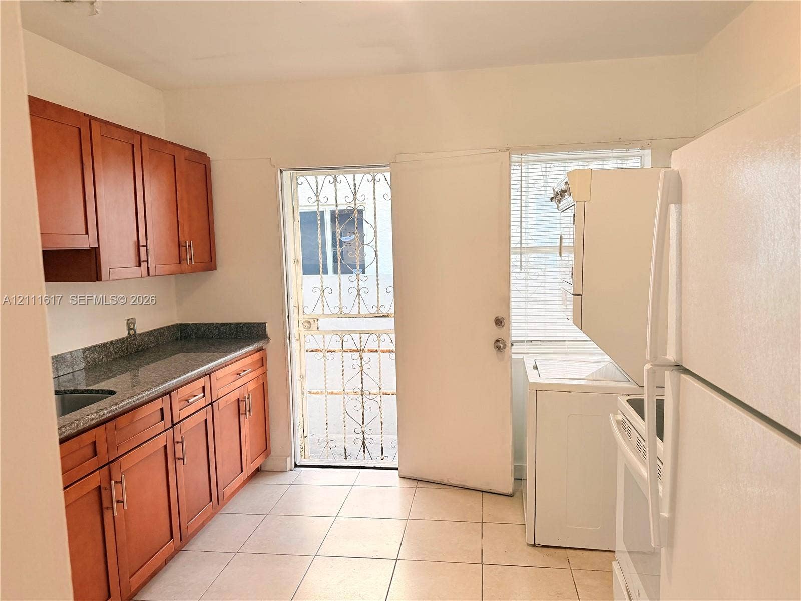 Kitchen featuring wood-finish cabinetry, stone-style countertops, ceramic tile flooring, and a metal security door