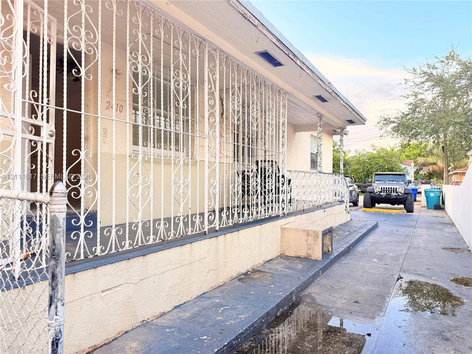 Exterior facade featuring decorative metal security grilles, covered porch area, and concrete driveway
