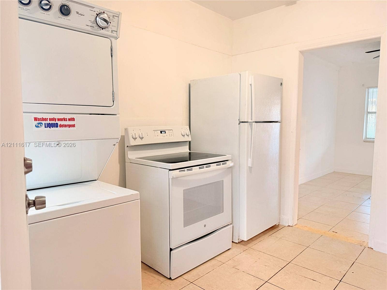 Stacked laundry unit, white electric range, and full-size refrigerator, featuring tile flooring