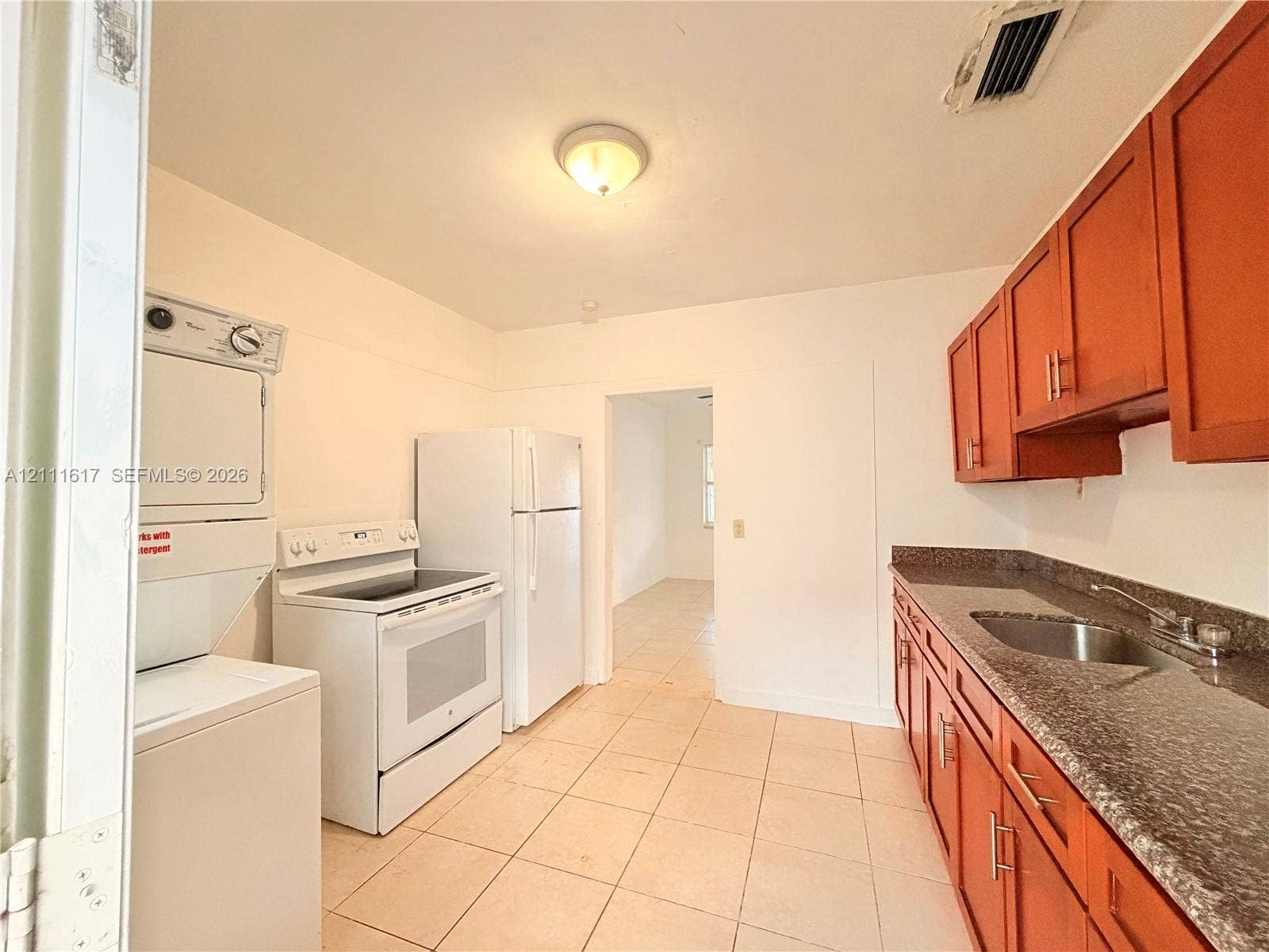 Kitchen featuring natural wood-finish cabinetry, stone-patterned countertops, stainless steel sink, ceramic tile flooring, and integrated laundry appliances