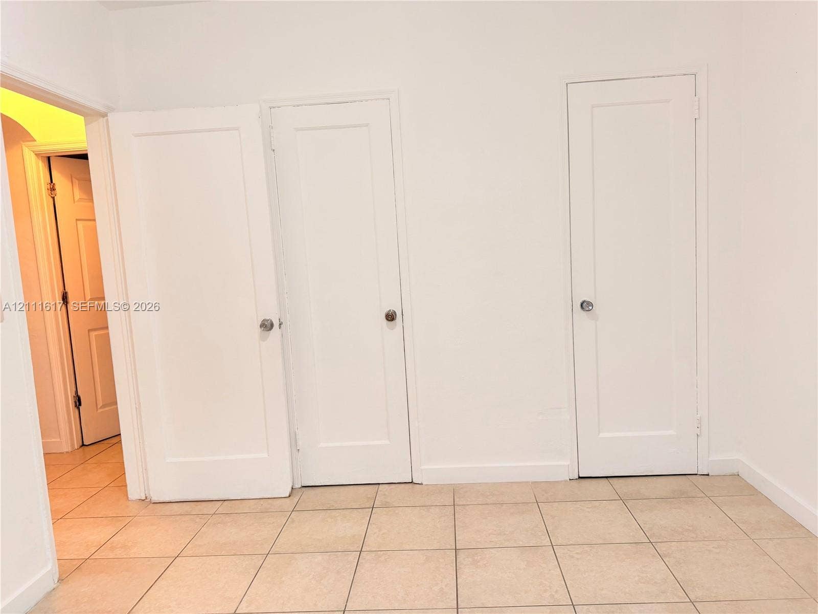 Neutral interior featuring ceramic tile flooring, three solid-core doors with chrome-finish hardware, and crisp white wall finishes