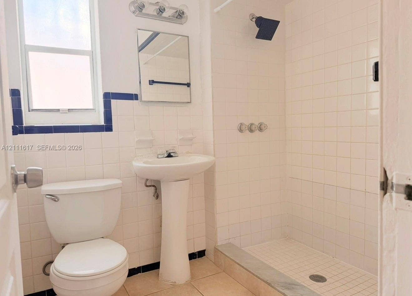 Bathroom featuring a white ceramic pedestal sink, tiled shower enclosure, square wall mirror, and chrome finish hardware