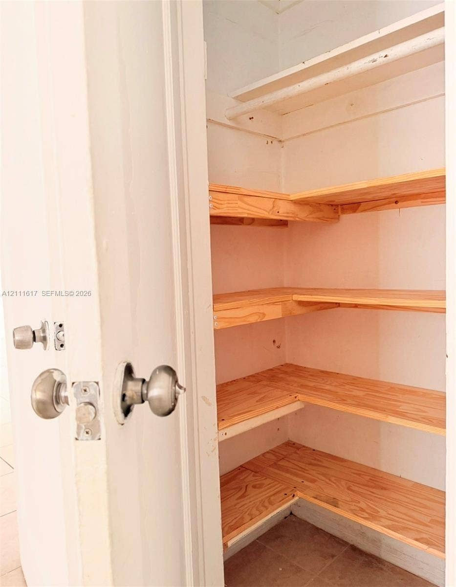 Storage closet featuring multi-level wooden shelving, a built-in overhead shelf with hanging rod, and brushed metal door hardware