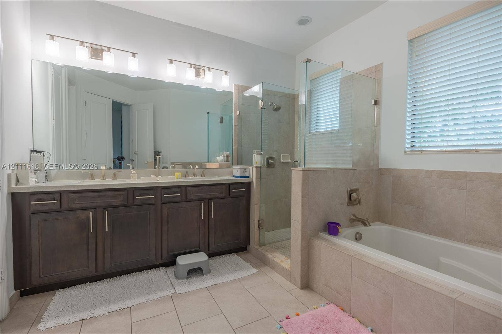 1423 SW 115th Avenue, #NA, Pembroke Pines, Pembroke Pines, FL 33025 Double vanity with dark cabinetry, large wall-to-wall mirror, glass-enclosed shower, and deep-soaking bathtub with tile surround