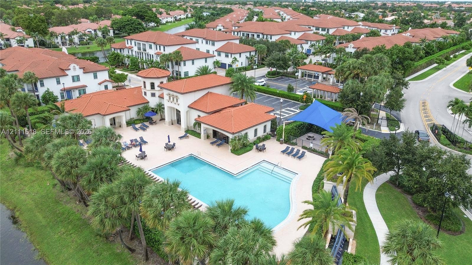 1423 SW 115th Avenue, #NA, Pembroke Pines, Pembroke Pines, FL 33025 Community swimming pool featuring a paved deck, terracotta tile roof clubhouse, and extensive landscaping with palm trees
