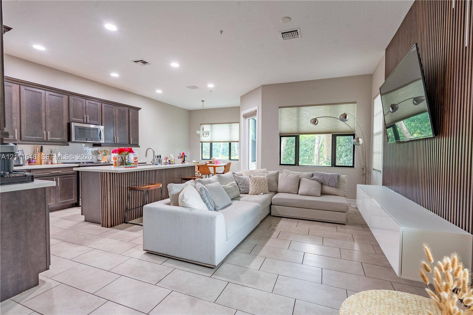 1423 SW 115th Avenue, #NA, Pembroke Pines, Pembroke Pines, FL 33025 Open-concept floor plan featuring dark wood-finish cabinetry, a kitchen island with vertical wood detailing, large-format tile flooring, and a floor-to-ceiling slatted wood accent wall