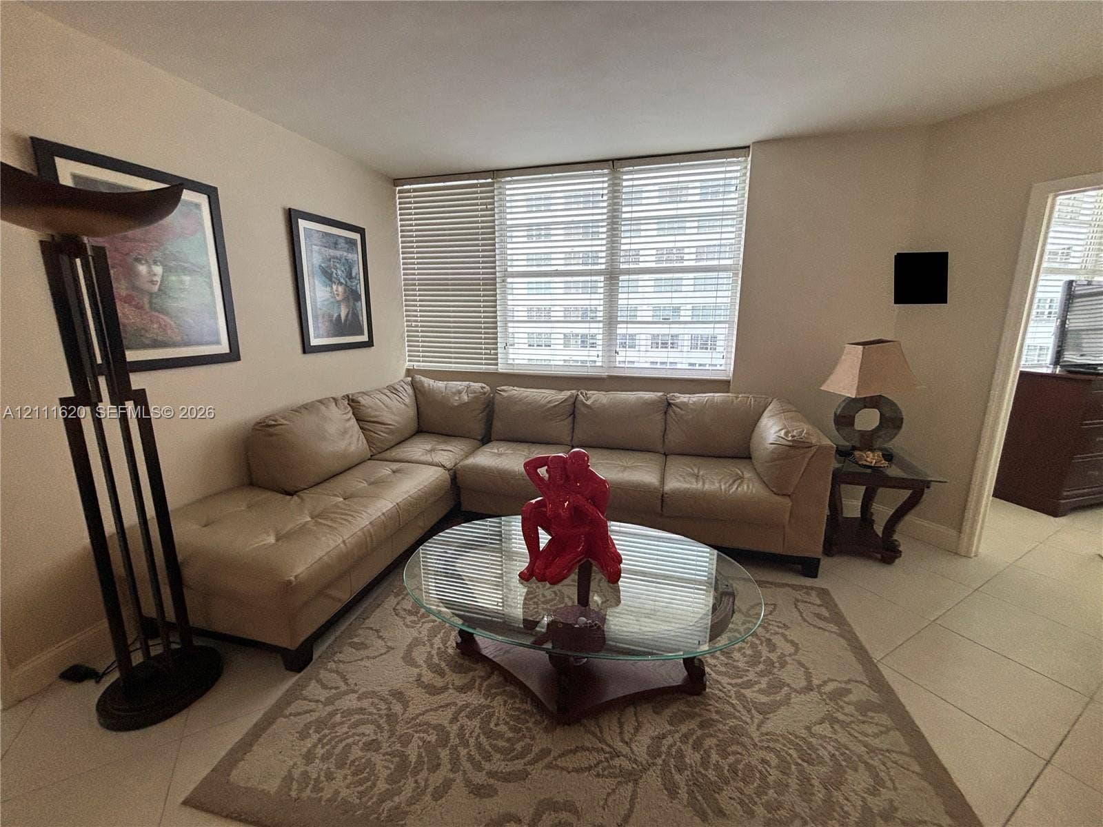Neutral-toned interior space featuring light-colored tile flooring and large windows with horizontal blinds