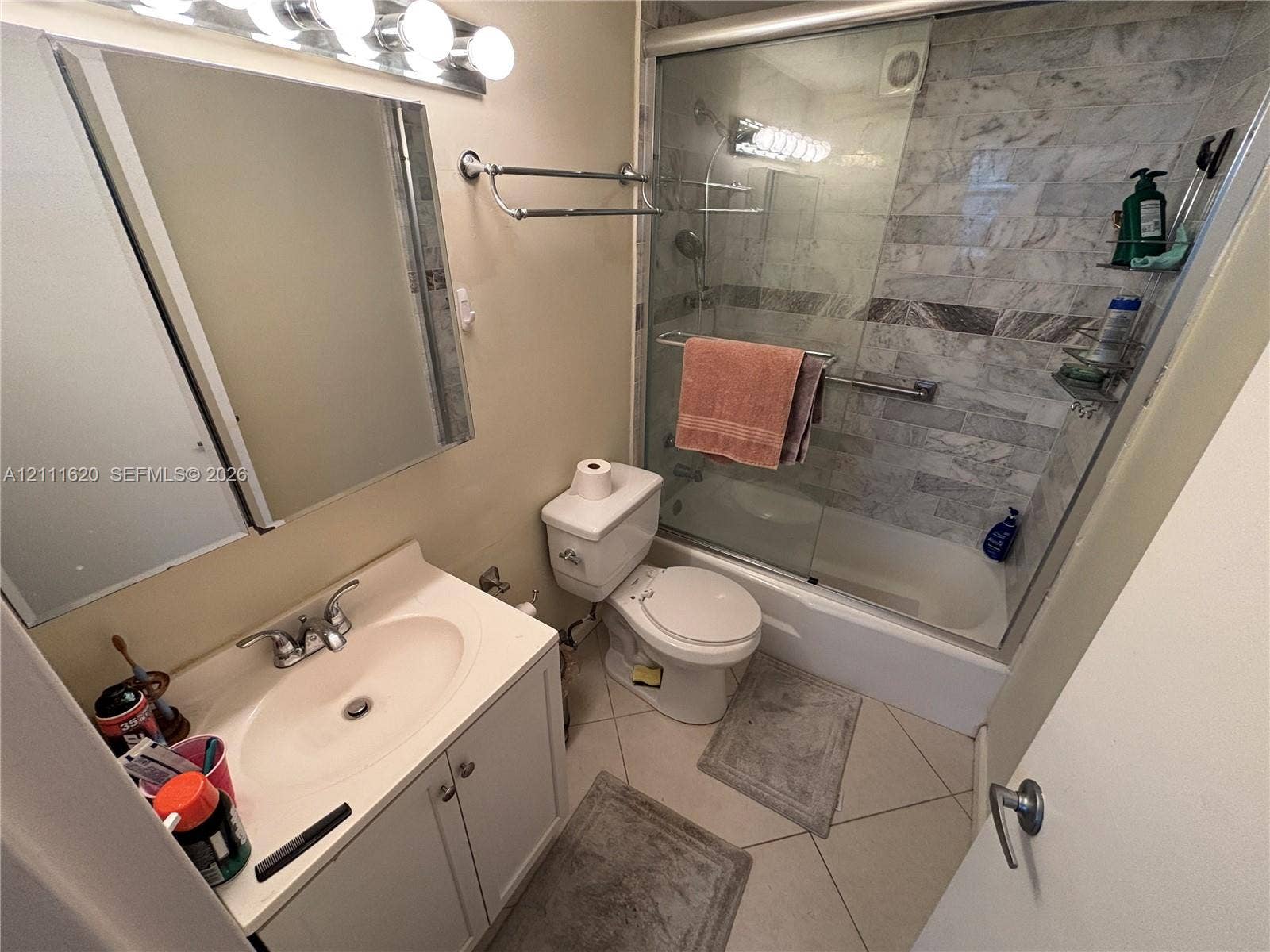 Bathroom featuring a vanity with an integrated sink, tri-light fixture, tiled shower surround, sliding glass shower doors, and ceramic tile flooring
