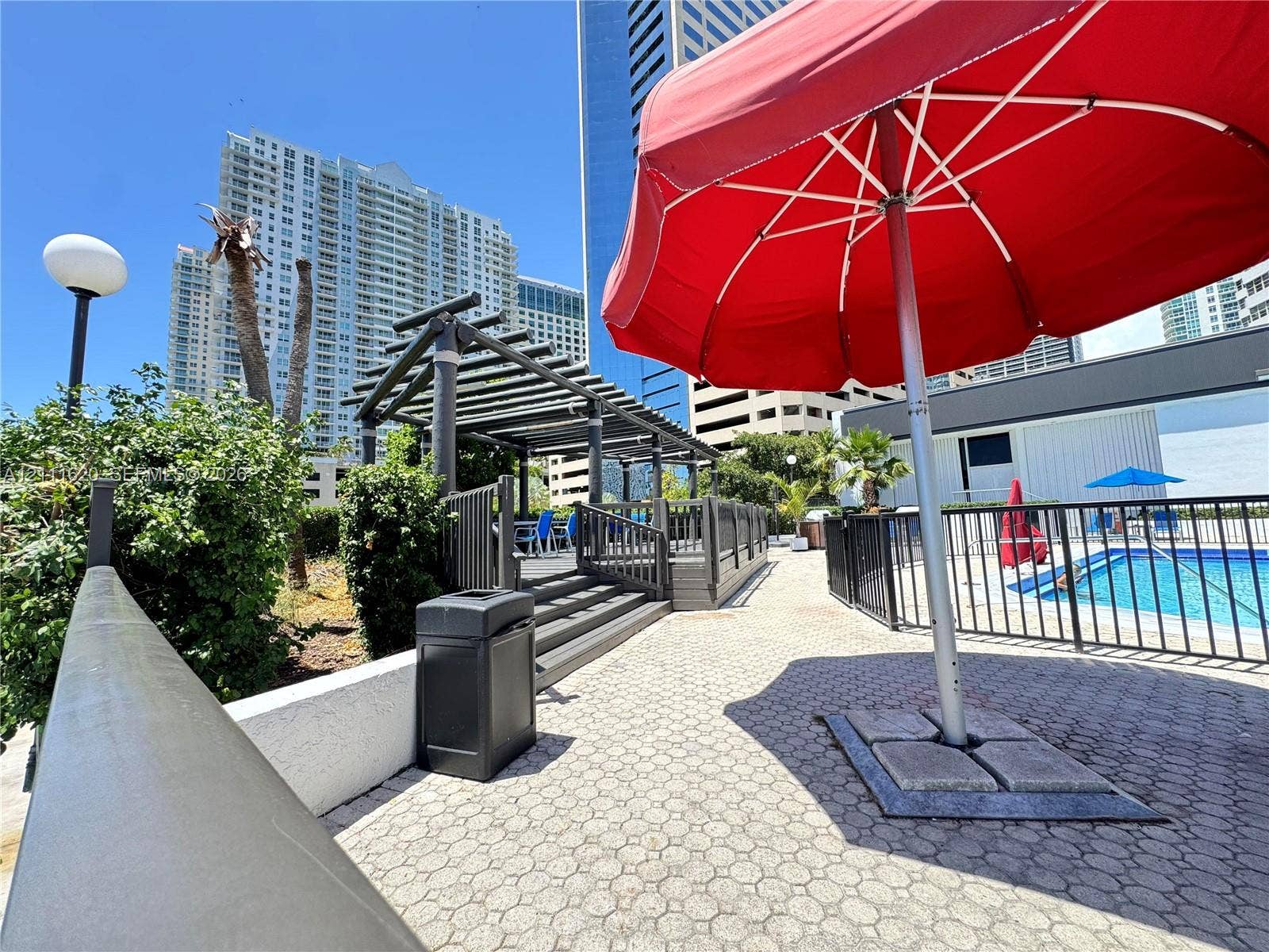 Outdoor terrace featuring a paved stone deck, a wooden pergola structure, and a swimming pool enclosed by black metal fencing