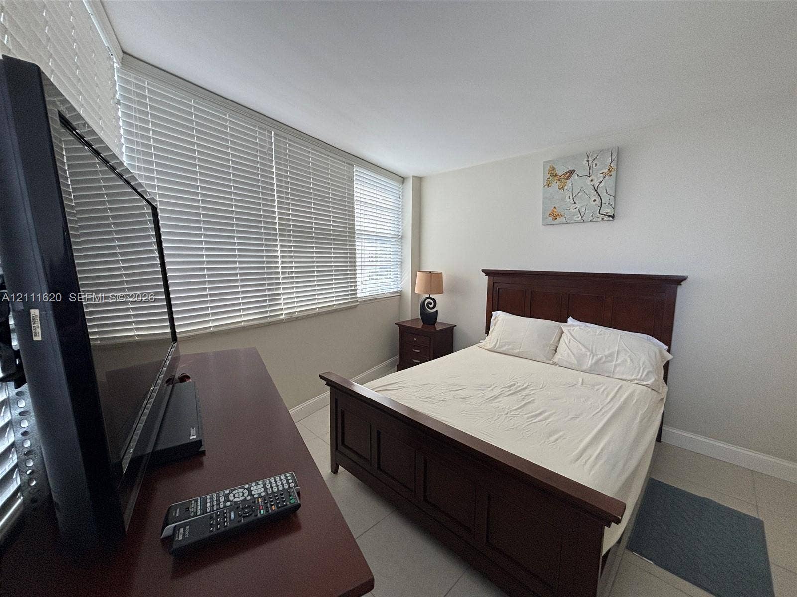 Neutral-toned interior space featuring light-colored tile flooring and large windows with horizontal blinds