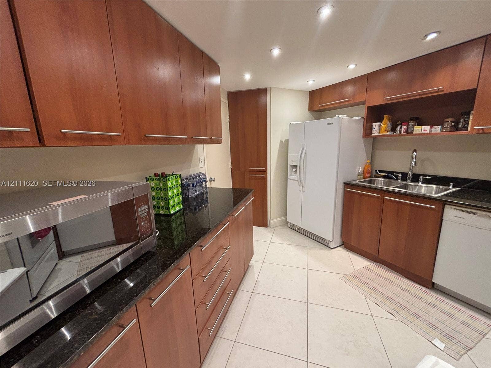 Kitchen featuring medium-tone wood cabinetry, dark stone countertops, recessed lighting, tile flooring, and integrated stainless steel and white appliances