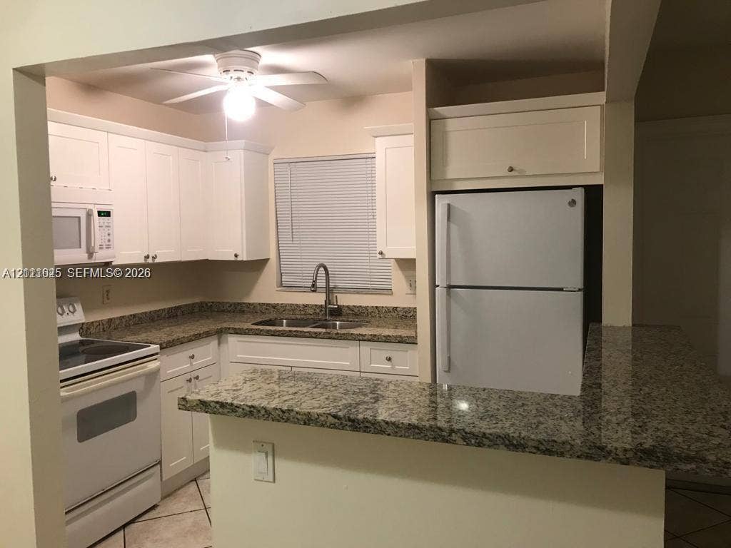 Kitchen featuring white cabinetry, stone-finish countertops, an integrated pass-through counter, a dual-basin sink with a gooseneck faucet, and tile flooring