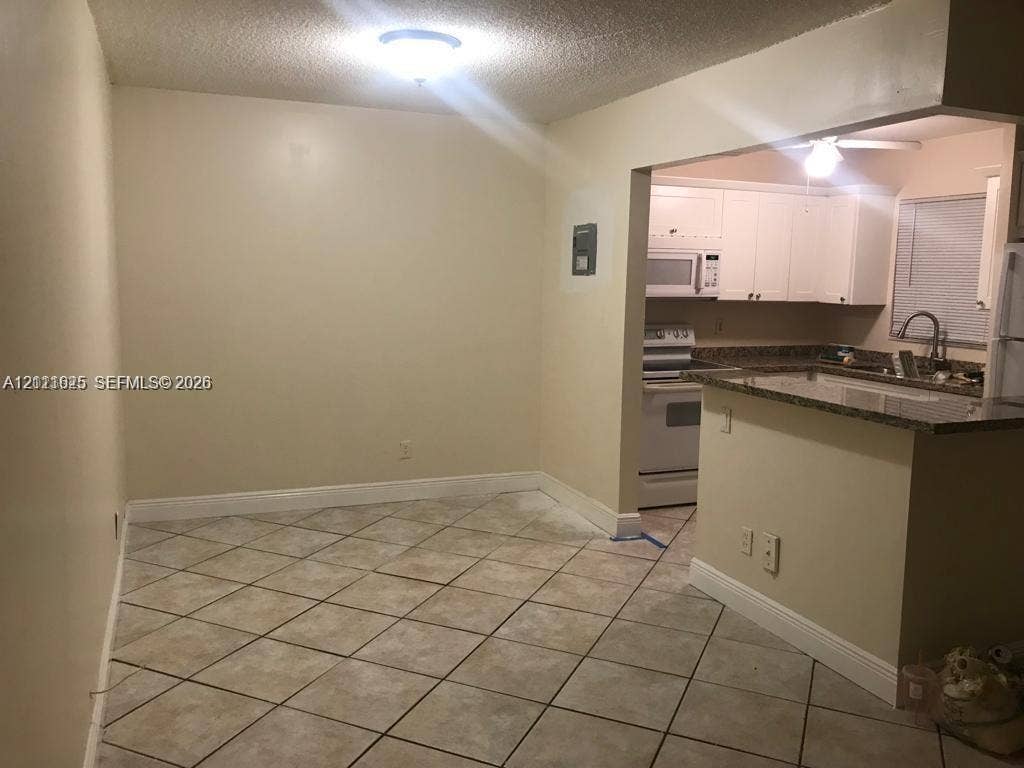 Ceramic tile flooring, white cabinetry, integrated microwave, stone-finish countertops, and a kitchen peninsula