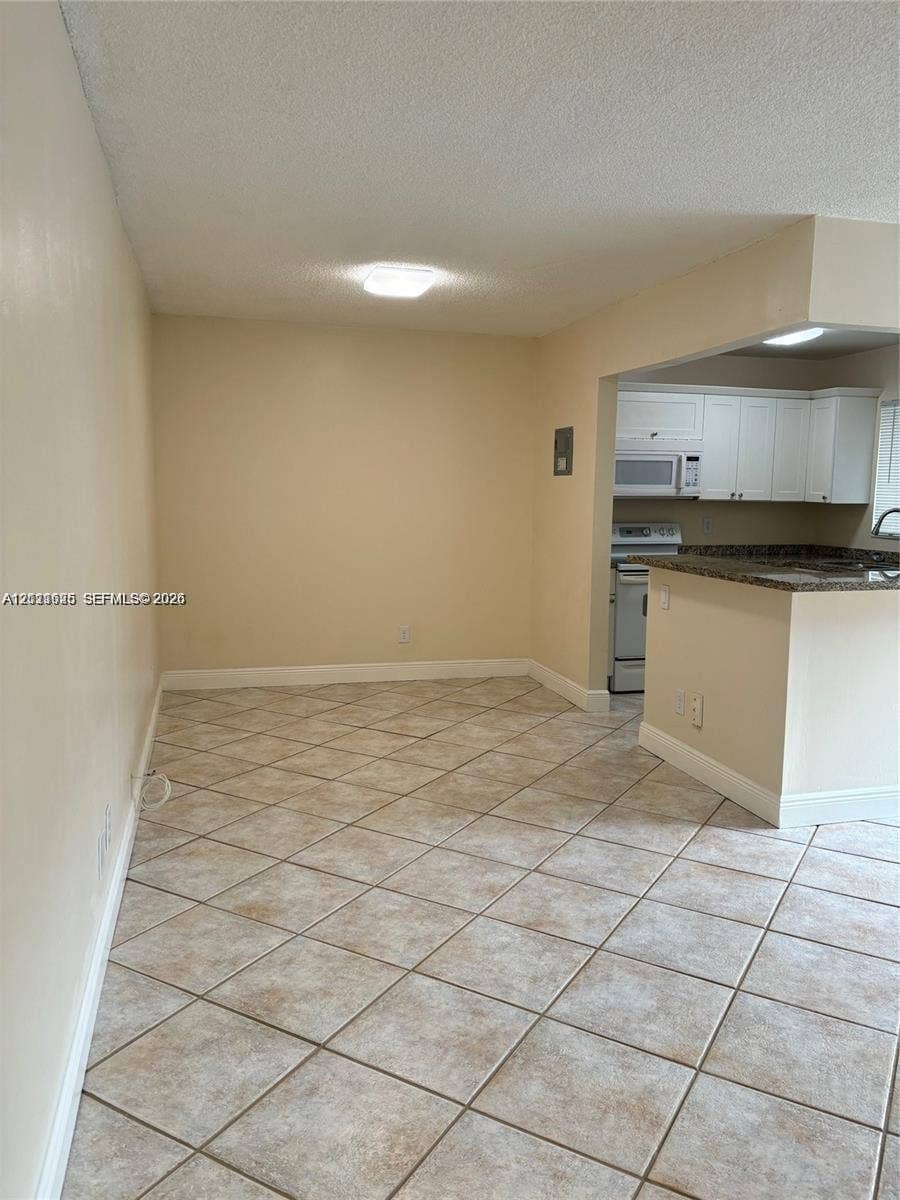 Ceramic tile flooring, kitchen featuring a breakfast bar, white cabinetry, built-in microwave, and stone-finish countertops