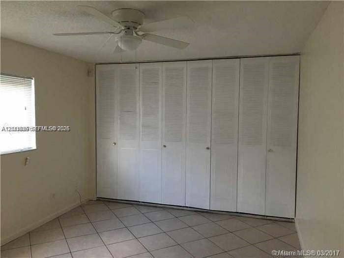 Floor-to-ceiling white louvered-style closet doors, neutral tile flooring, and a ceiling-mounted fan