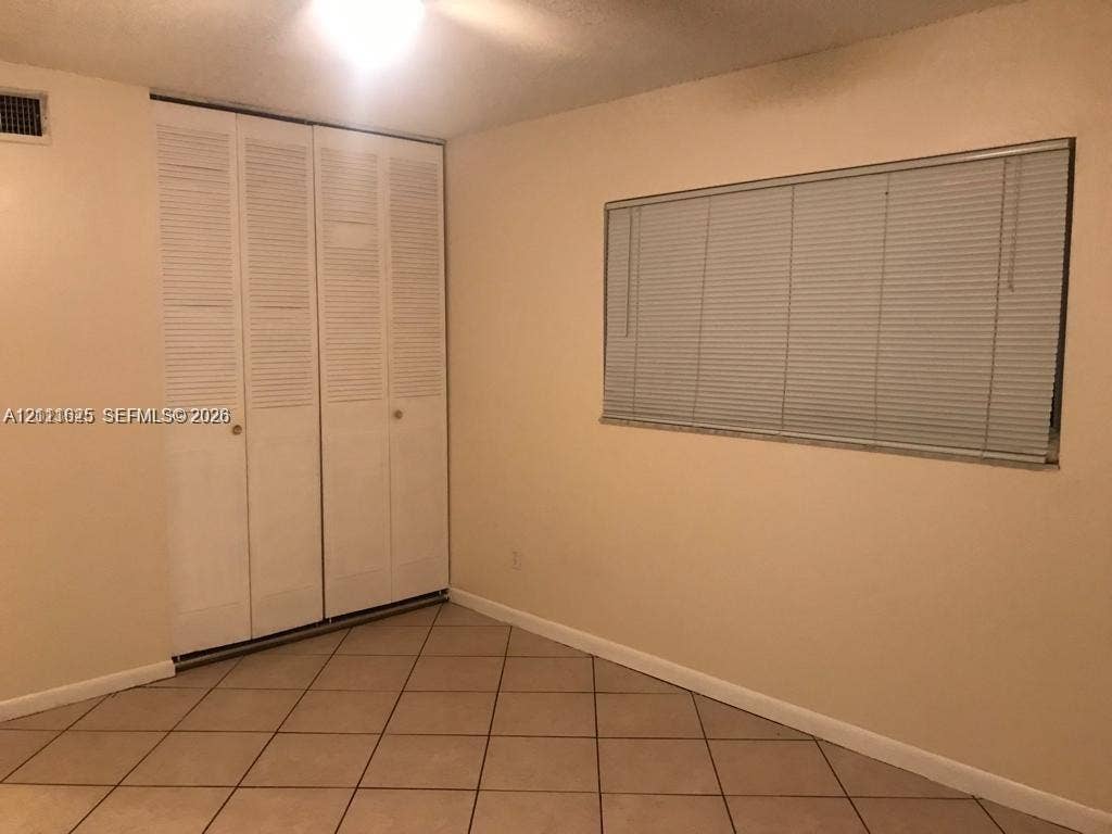 Neutral-toned room featuring tiled flooring, a set of floor-to-ceiling bi-fold closet doors, and a rectangular window fitted with horizontal blinds