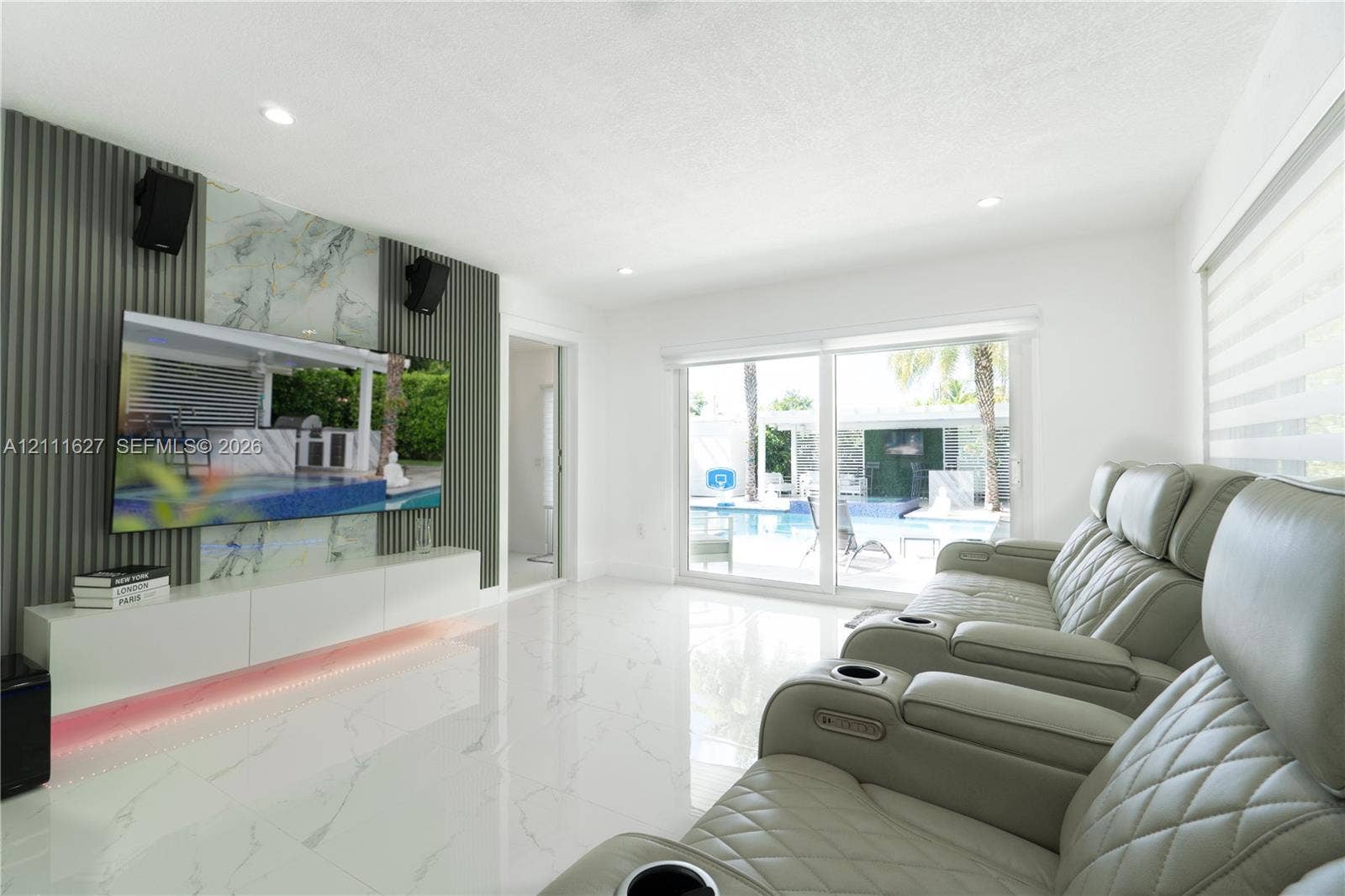 Polished stone-finish flooring, custom accent wall featuring vertical slats and a natural stone-finish inset, integrated low-profile cabinetry with under-cabinet lighting, and expansive sliding glass doors