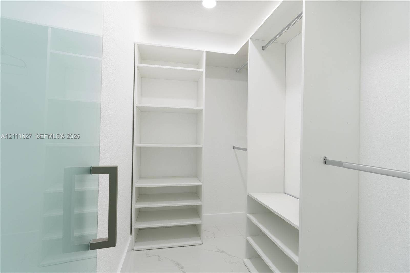Custom walk-in closet featuring white built-in shelving, floor-to-ceiling storage units, multiple metal hanging rods, and stone-finish tile flooring