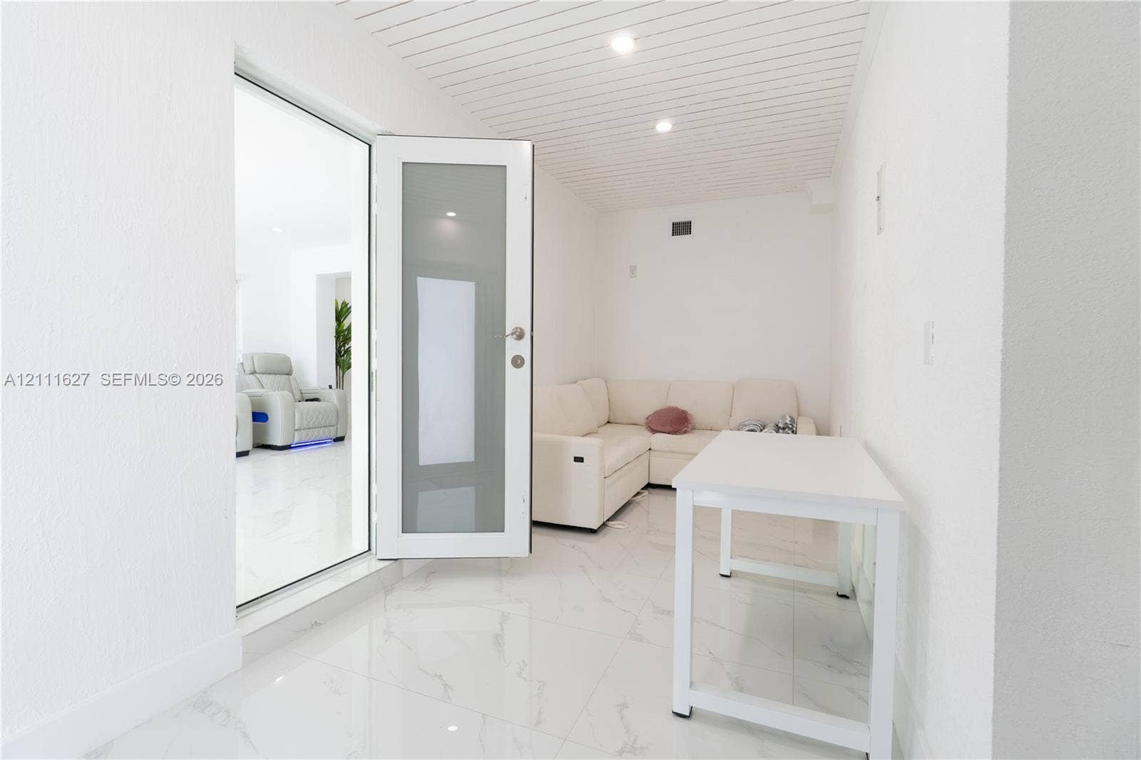 Interior space featuring polished white tile flooring, a frosted glass-panel door, and a white beadboard ceiling with recessed lighting