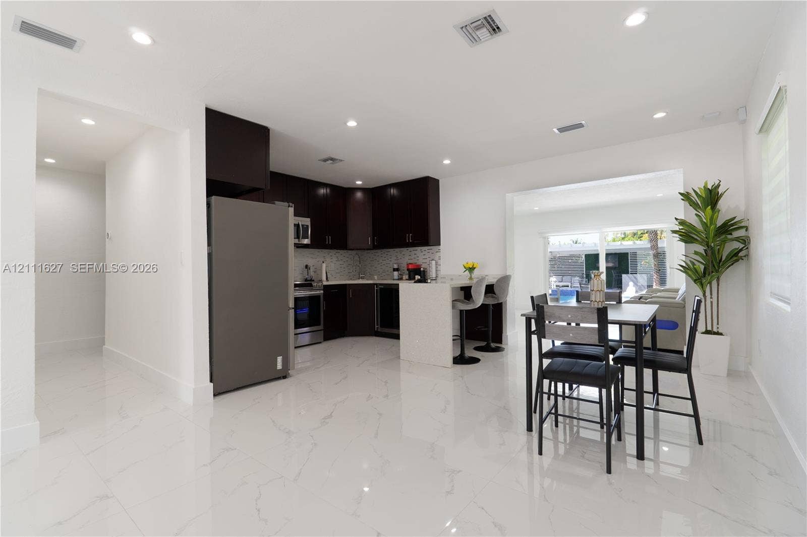 Kitchen featuring dark-toned cabinetry, a stone-finish countertop island with a breakfast bar, stainless steel appliances, a mosaic-tile backsplash, and polished stone-finish flooring