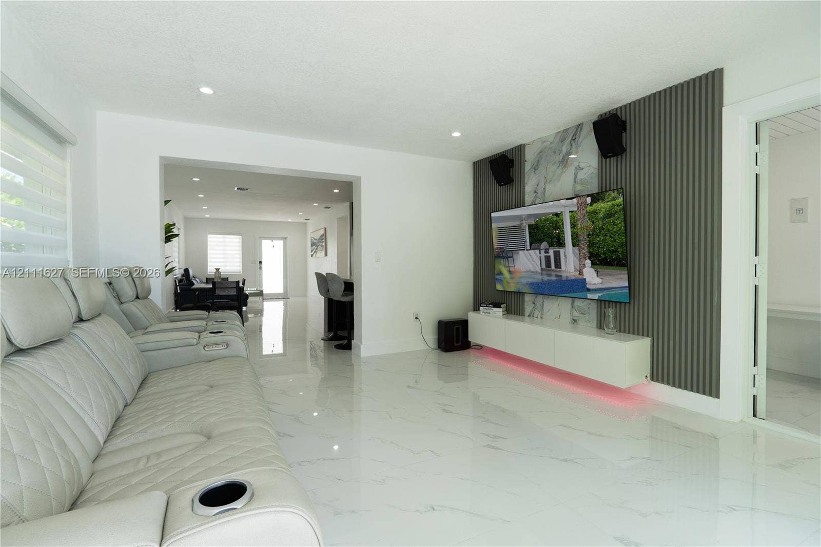Living area featuring polished tile flooring, a wall-mounted floating media cabinet, and a decorative accent wall with vertical slat paneling and stone-finish cladding