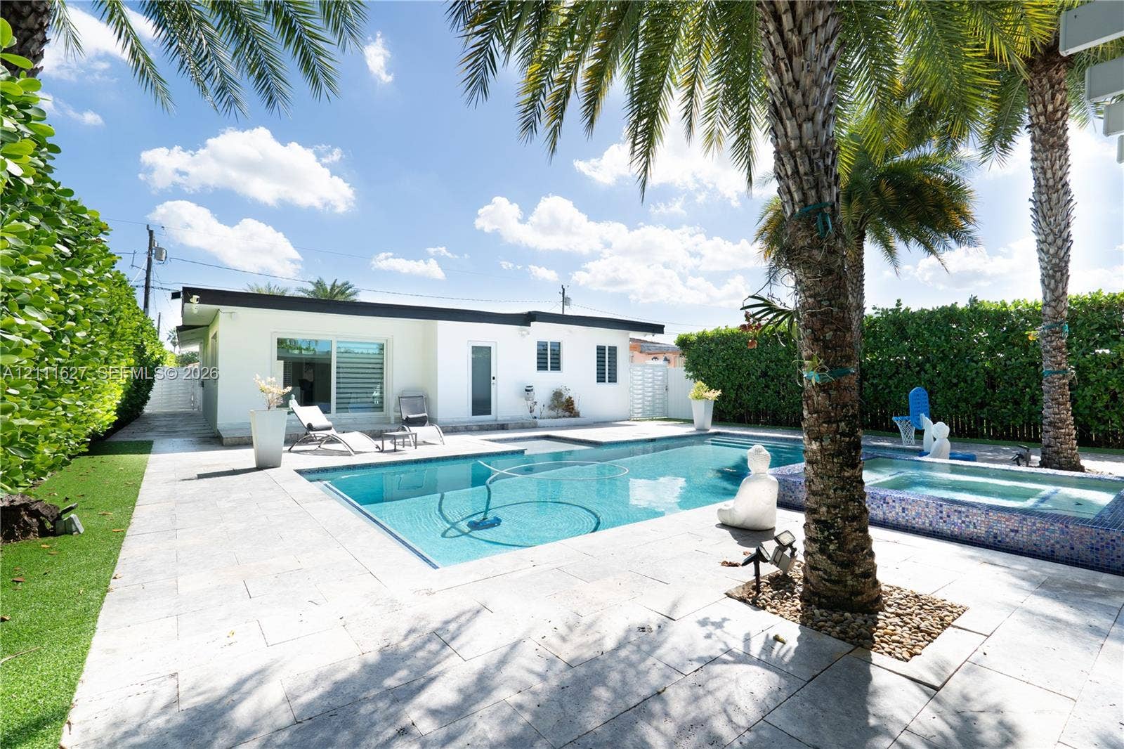 Outdoor swimming pool with integrated spa, stone-tile decking, mature palm trees, and perimeter privacy hedges