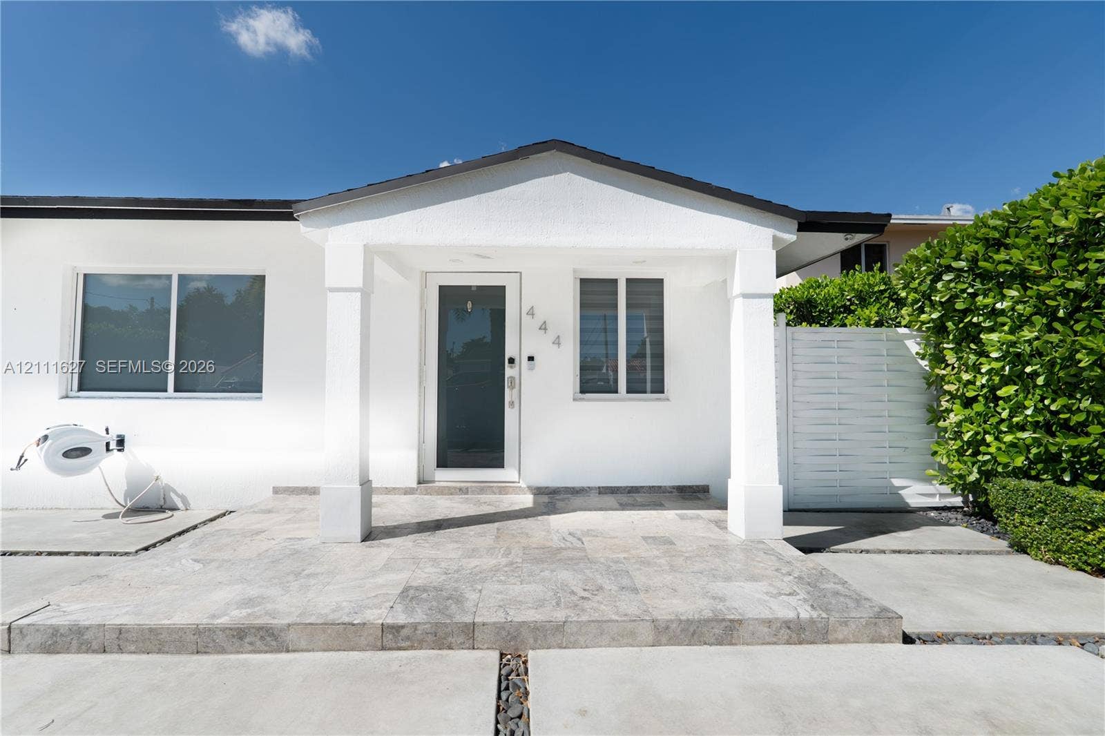 Exterior facade featuring a covered entryway, stone-tile porch, full-glass front door, and white privacy fencing