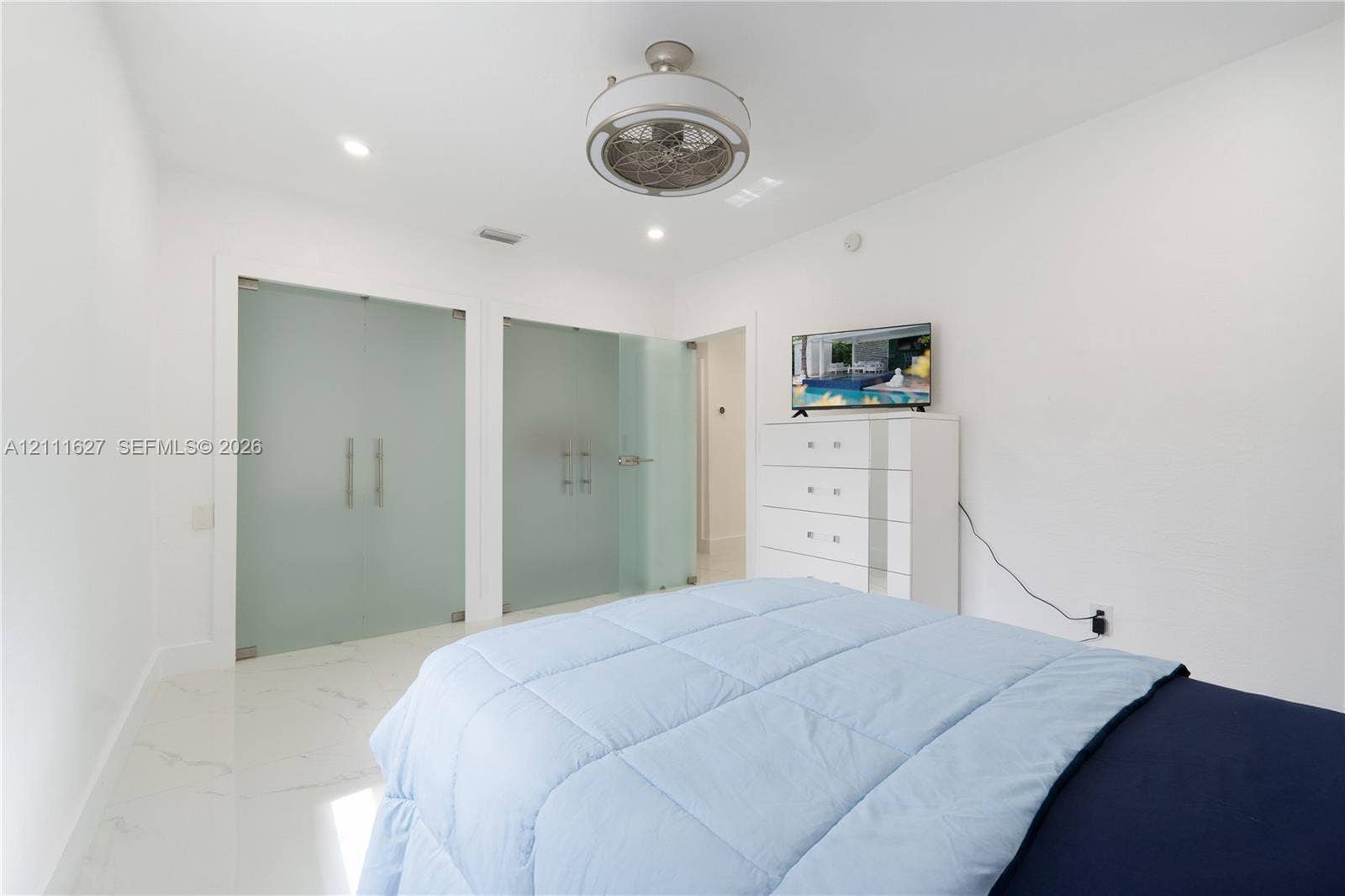 Room featuring white stone-finish flooring, recessed lighting, a modern circular ceiling fan, and two glass-panel doors with matte metal hardware