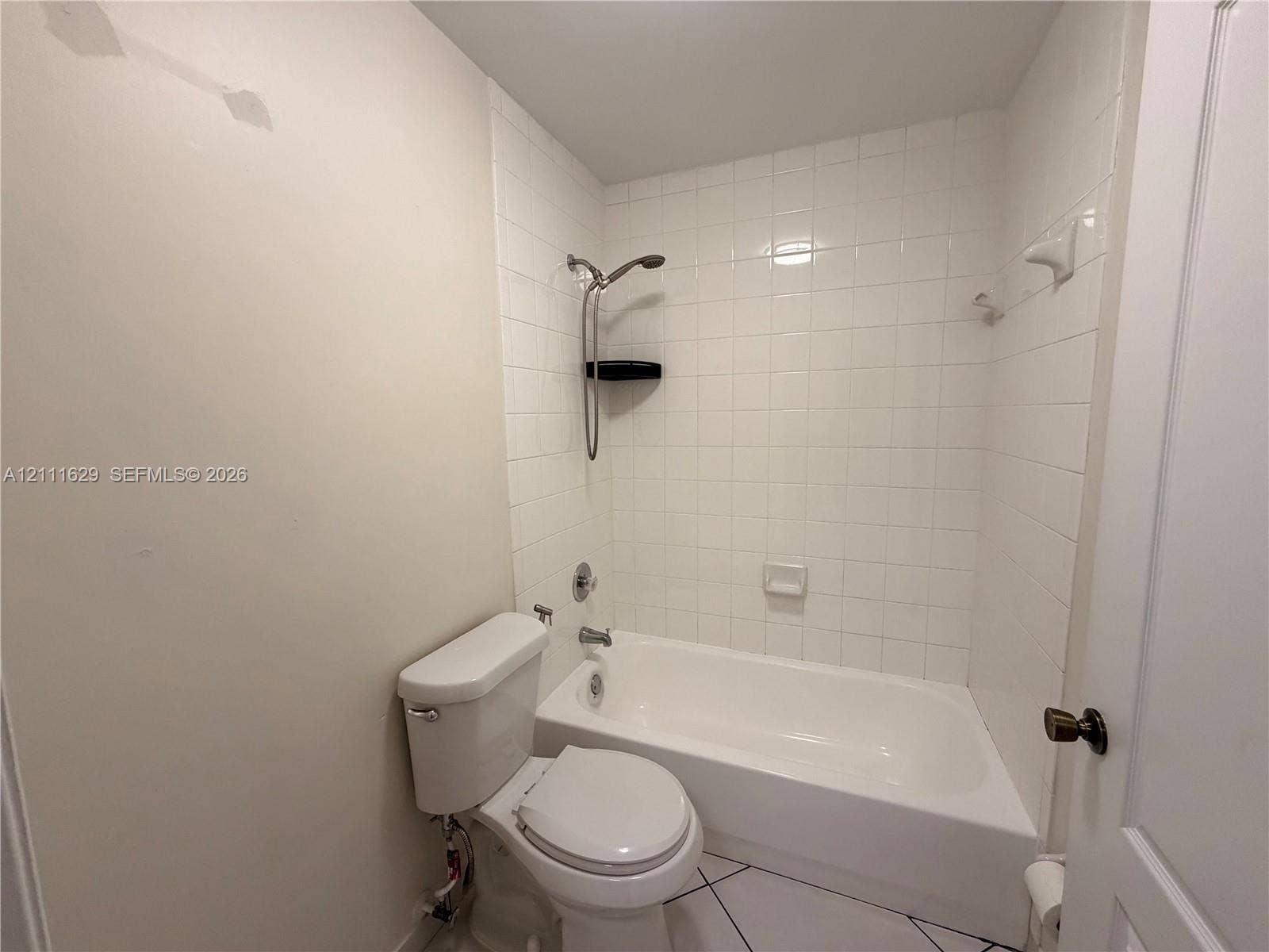 Bathroom featuring a porcelain tub and shower combination with white wall tile, a ceramic toilet, and tile flooring