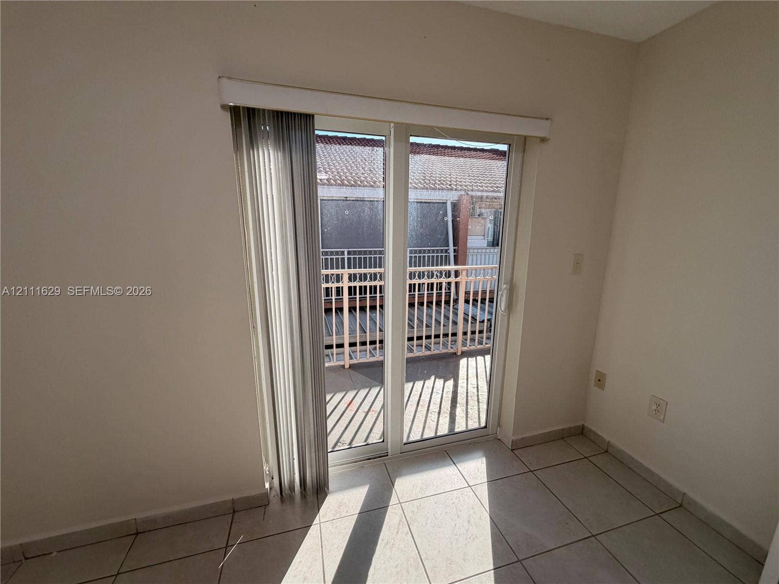 Double sliding glass doors with vertical blinds, tile flooring, and access to a balcony with metal railing