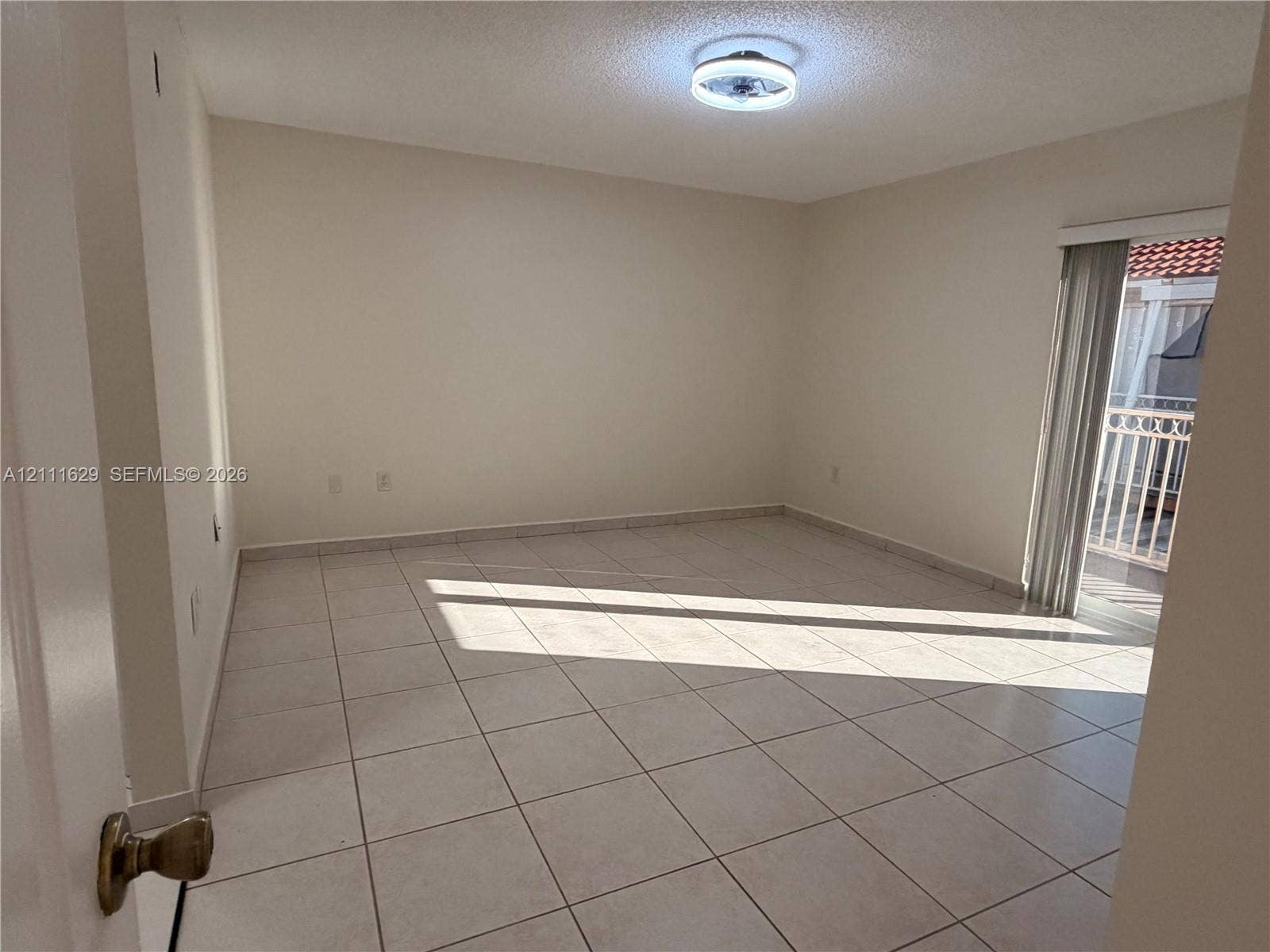 Room featuring neutral tile flooring, a flush-mount circular ceiling light, and sliding glass doors with access to an exterior balcony