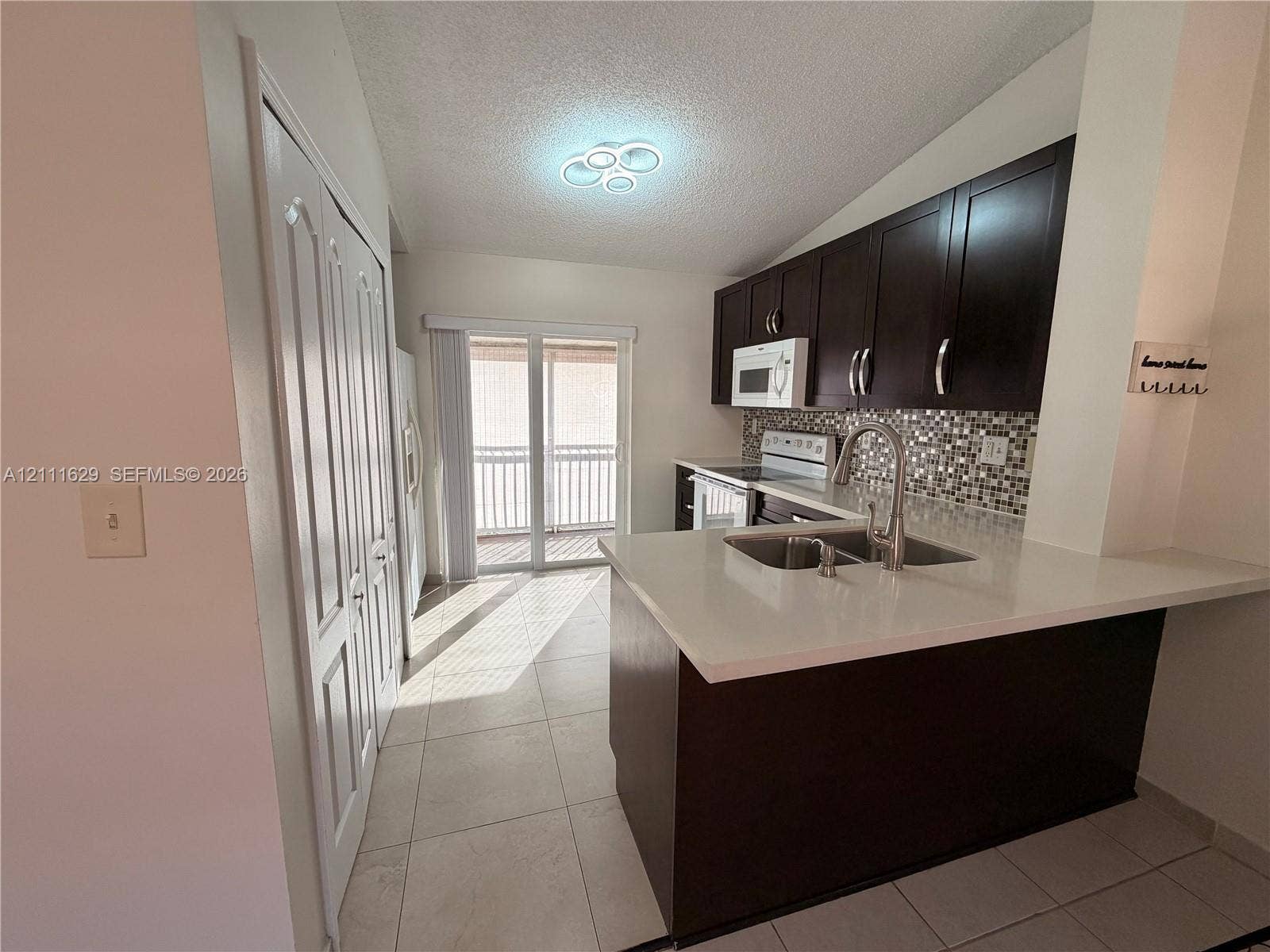 Kitchen featuring dark cabinetry, quartz countertops, mosaic tile backsplash, double-basin stainless steel sink with pull-down faucet, and tile flooring