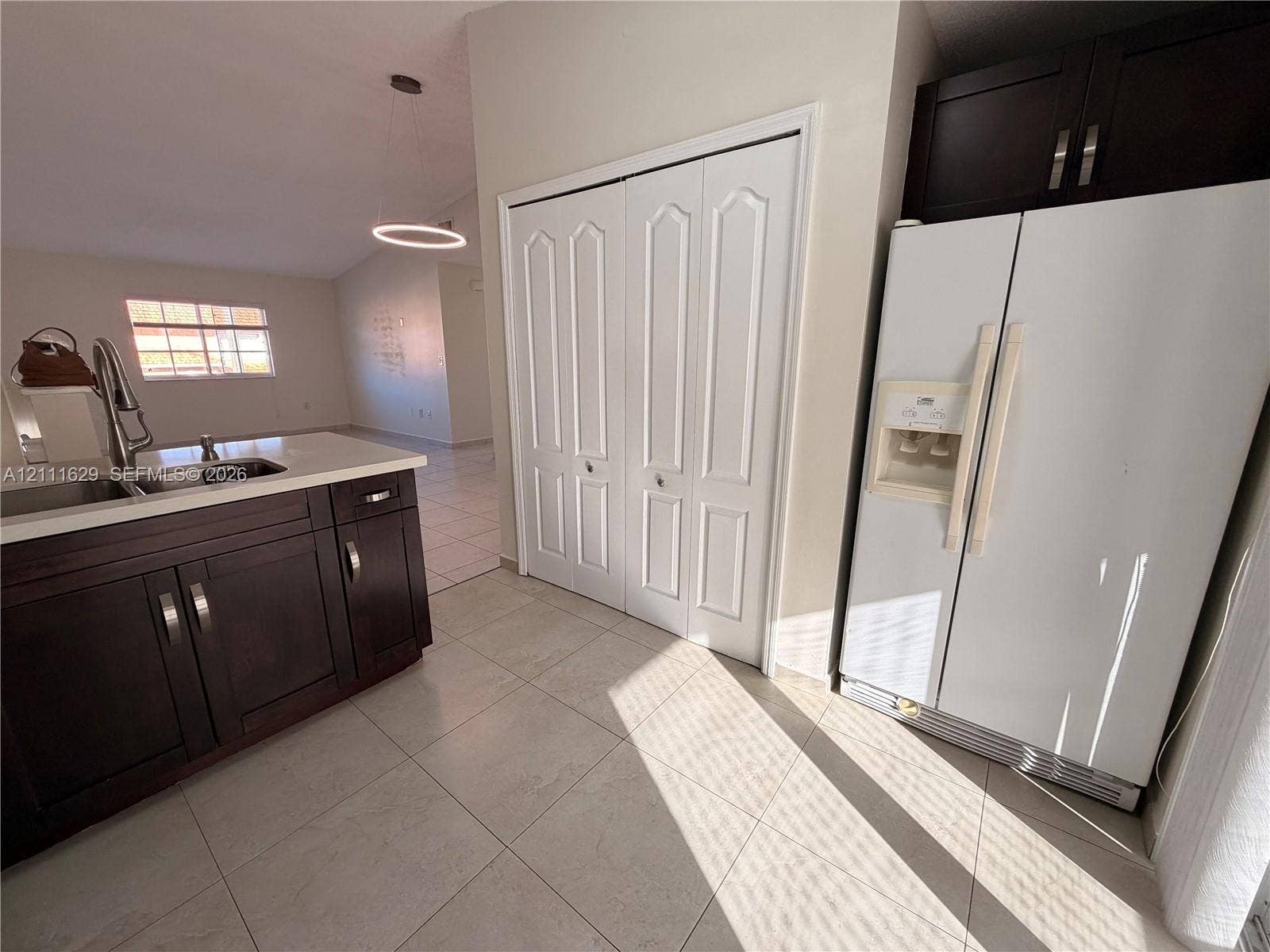 Kitchen featuring dark wood-finish cabinetry, solid-surface countertops, dual-basin stainless steel sink with high-arc faucet, tile flooring, and floor-to-ceiling bi-fold closet doors