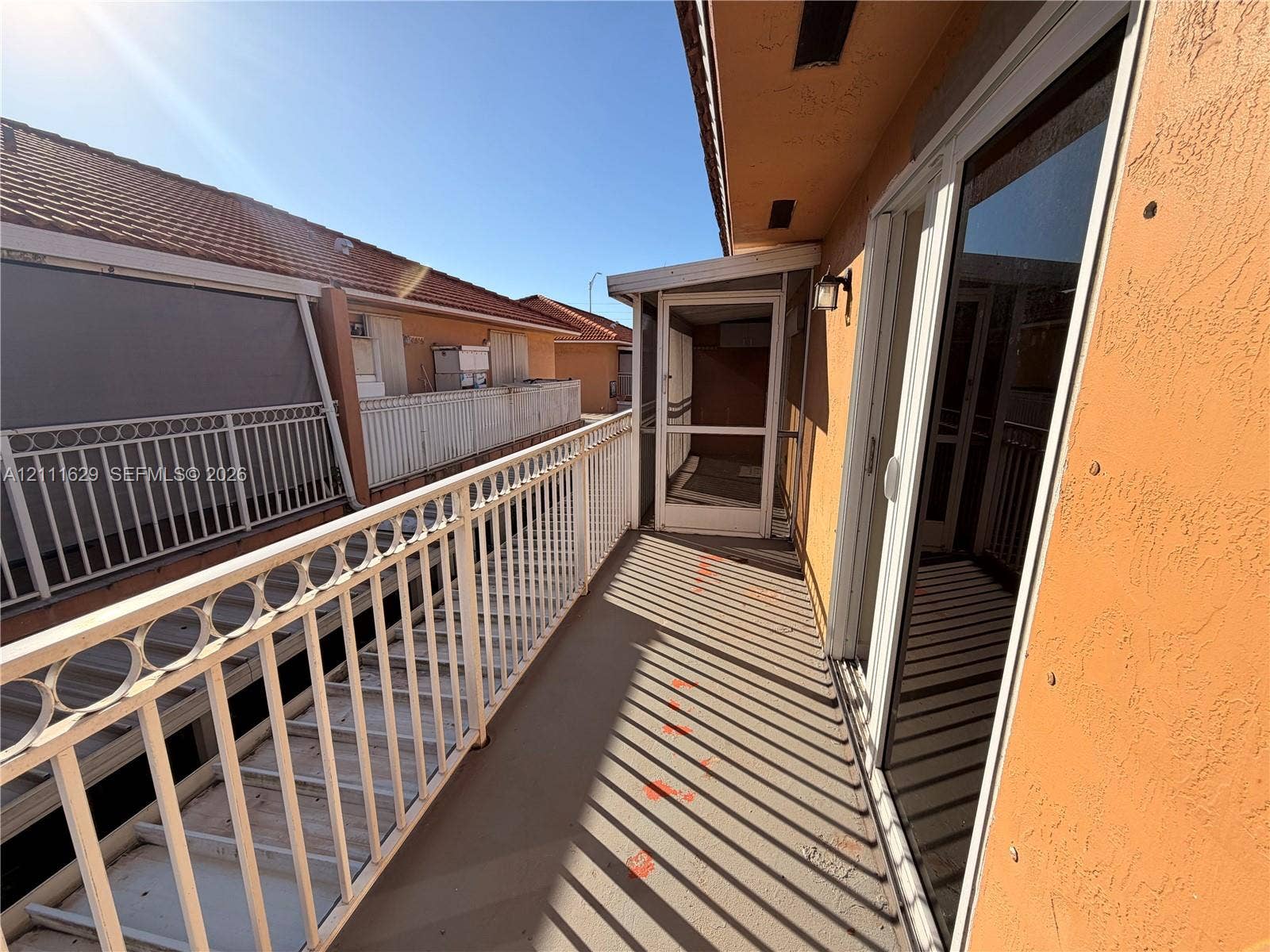 Exterior balcony featuring white metal railings, a screened-in enclosure, and sliding glass door entry