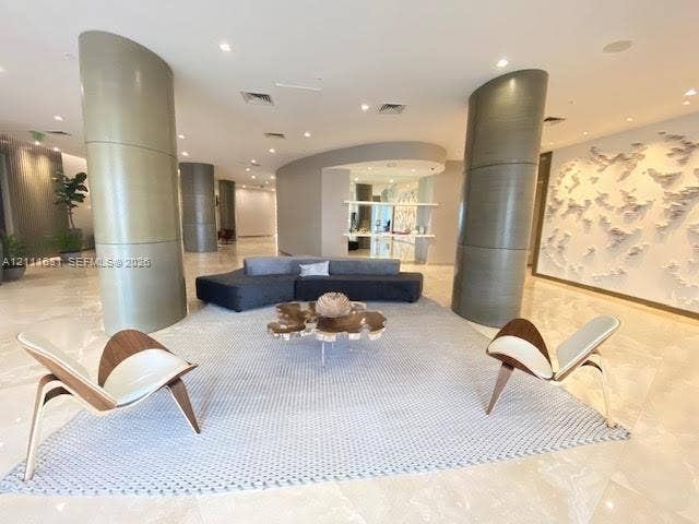 Open-concept lobby featuring polished stone flooring, curved architectural pillars, recessed lighting, and a textured decorative feature wall