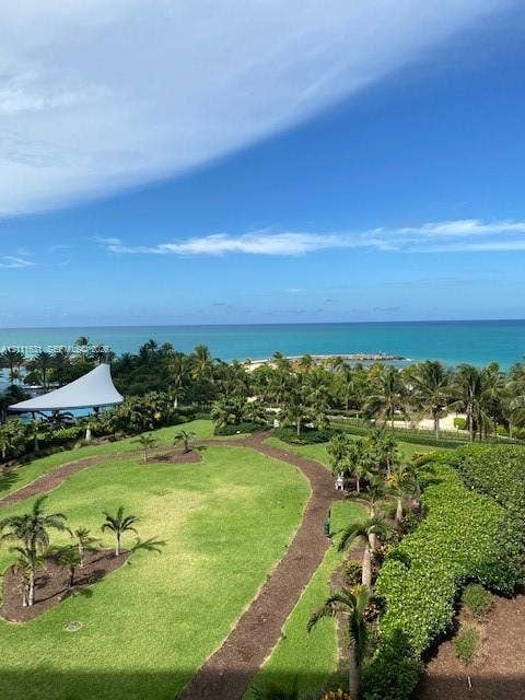 Expansive grounds featuring manicured turf, mature palm trees, meandering garden paths, and an ocean horizon backdrop