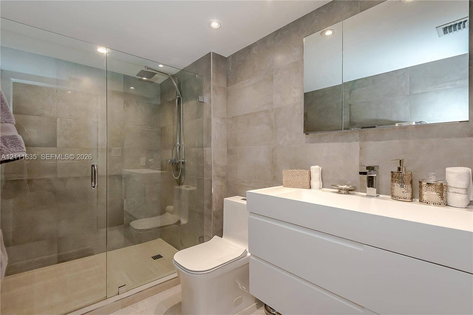 90 Alton Road, #2410, Miami Beach, FL 33139 Bathroom featuring large-format neutral wall tile, walk-in glass shower enclosure with rainfall showerhead, white wall-mounted vanity, undermount sink with chrome faucet, and rectangular medicine cabinet