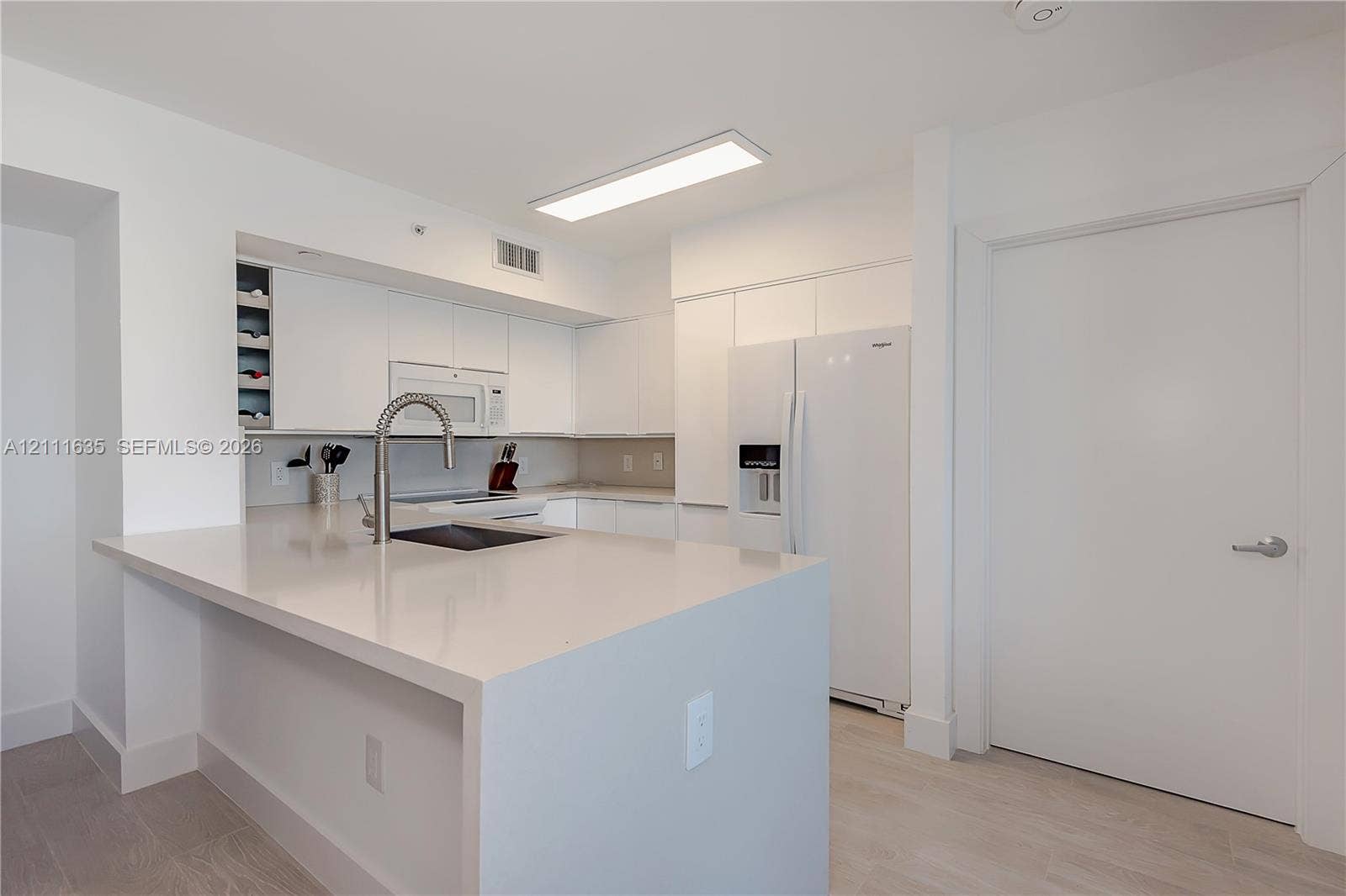 90 Alton Road, #2410, Miami Beach, FL 33139 Kitchen featuring flat-panel white cabinetry, solid surface countertops, built-in wine rack, integrated microwave, and wood-finish flooring